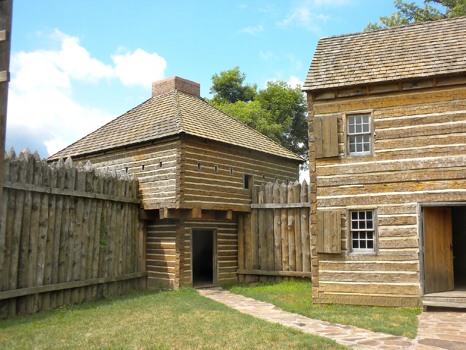 Reconstructed log buildings behind a wooden stockade fence on a green lawn