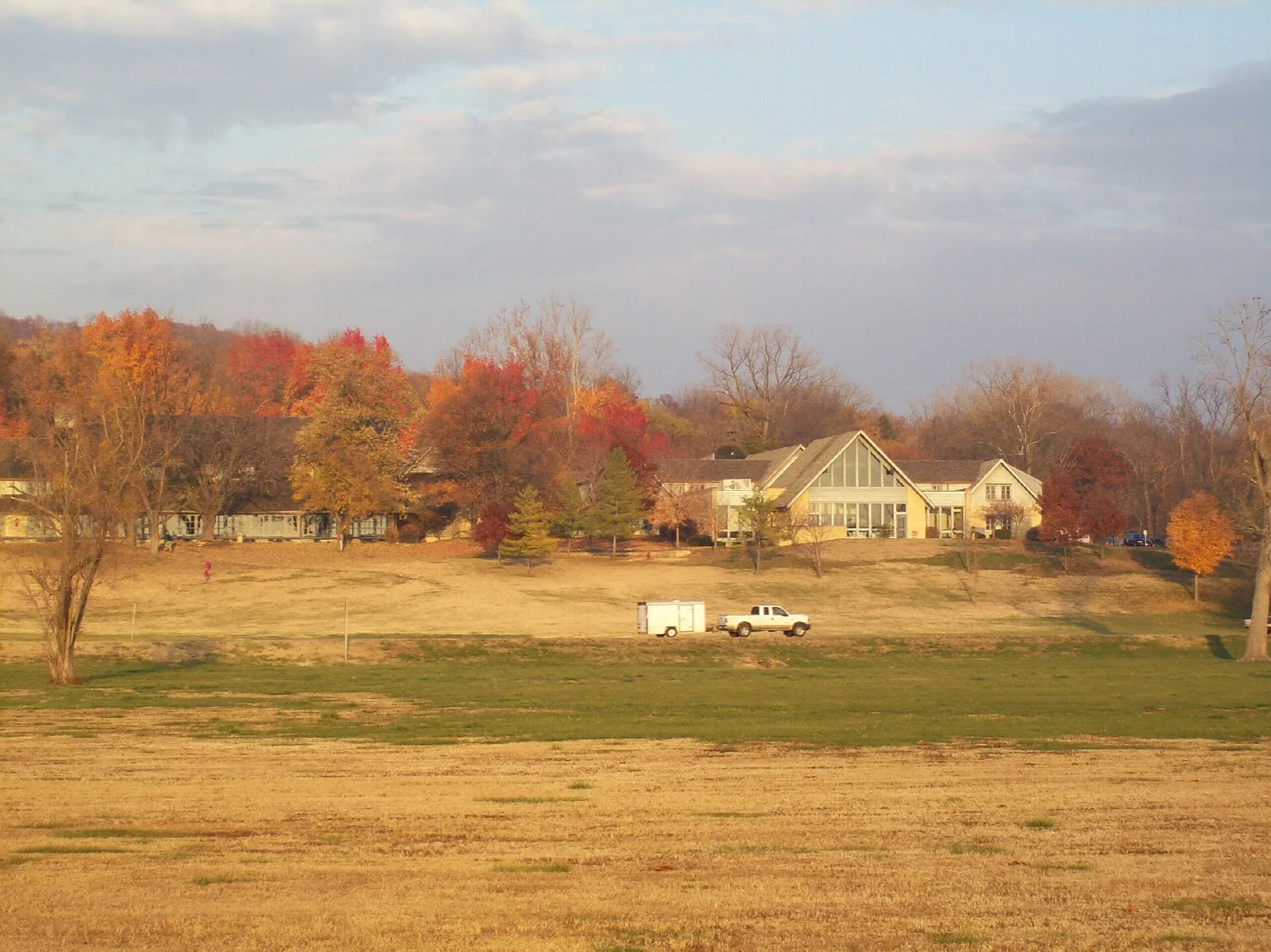 Lodge-style building beyond an autumn field with trees in red and orange