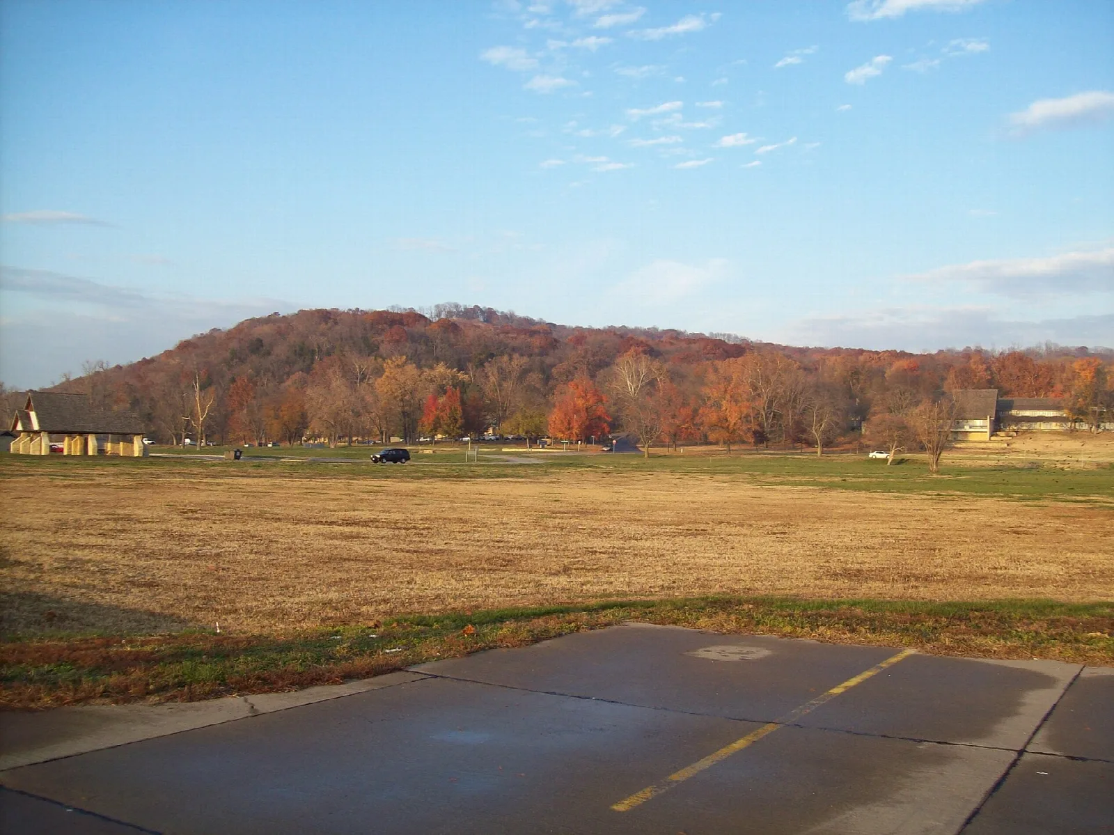 Wooded hill in autumn color above an open grass field and paved road