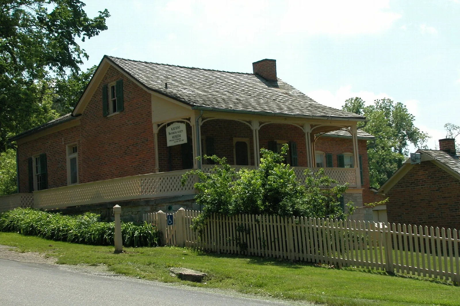 Two-story brick house with a front porch and a white picket fence beside a road