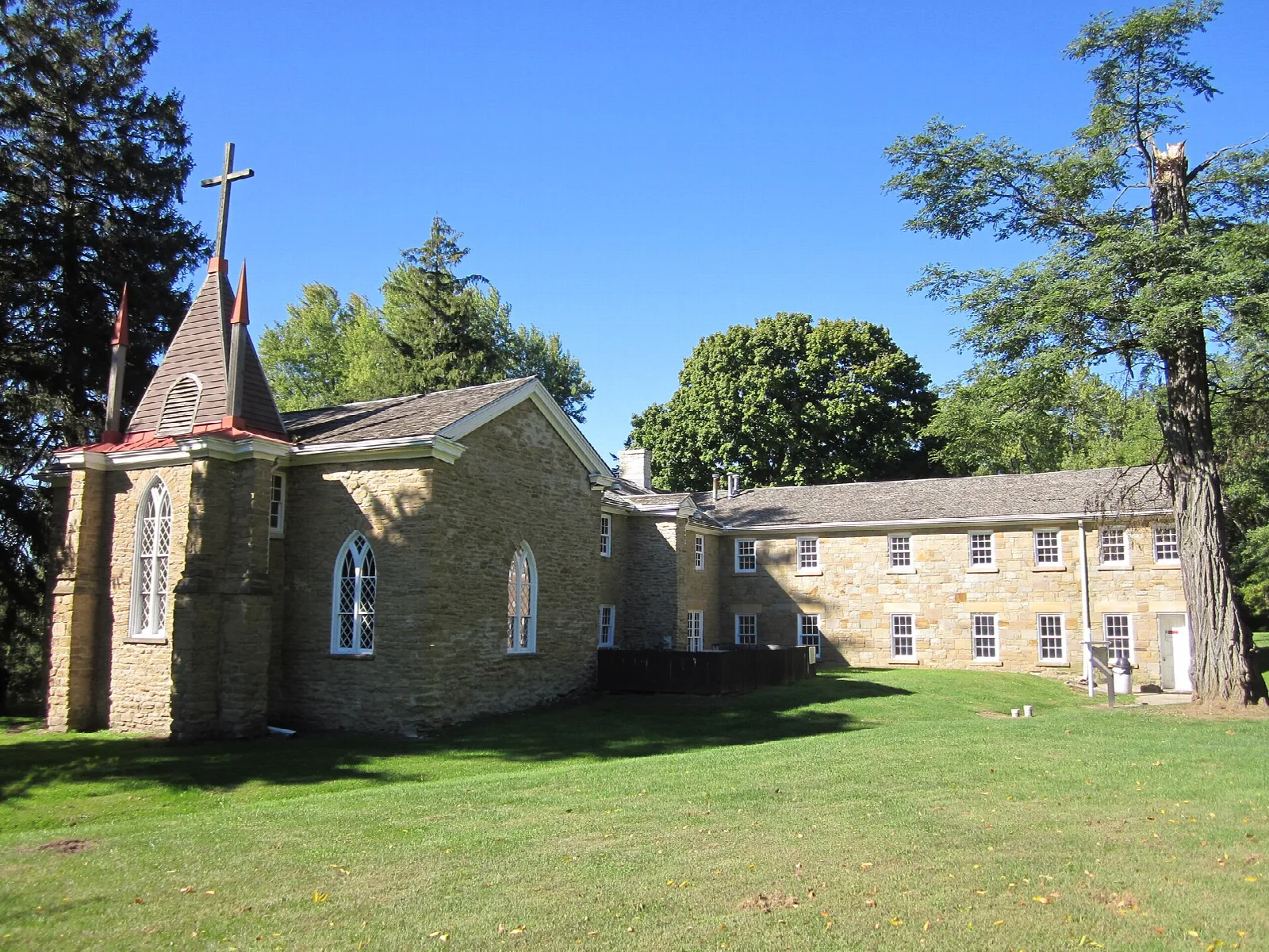 Stone chapel with a small steeple and a long stone building on a green lawn
