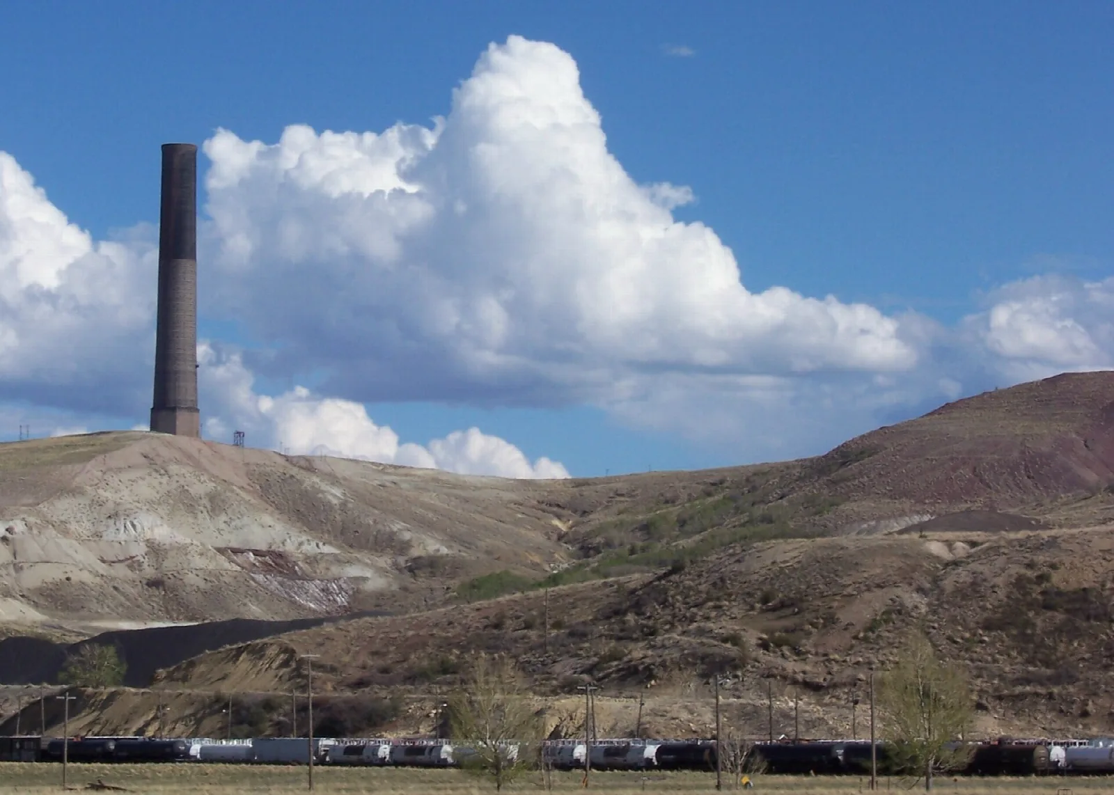 Tall dark brick smokestack on a hill under big white clouds