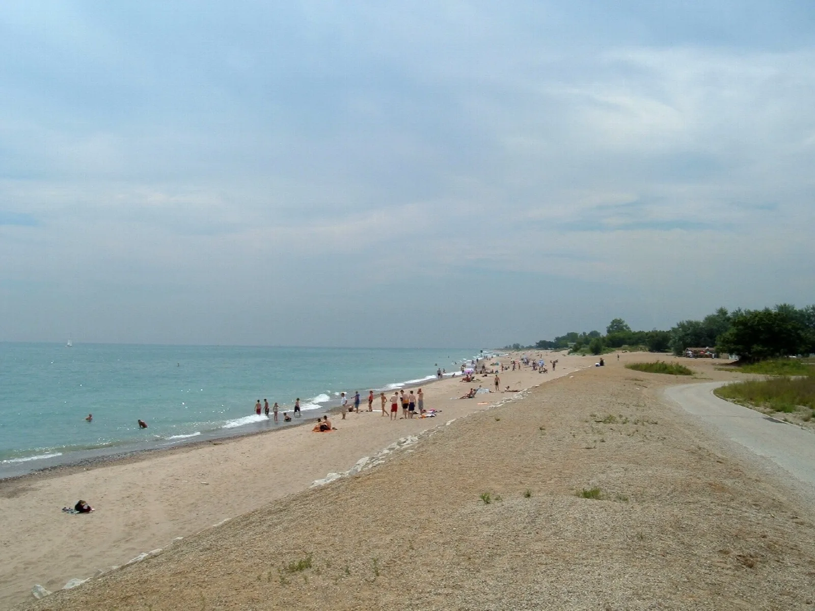 Wide sandy beach along a lake with swimmers in the distance