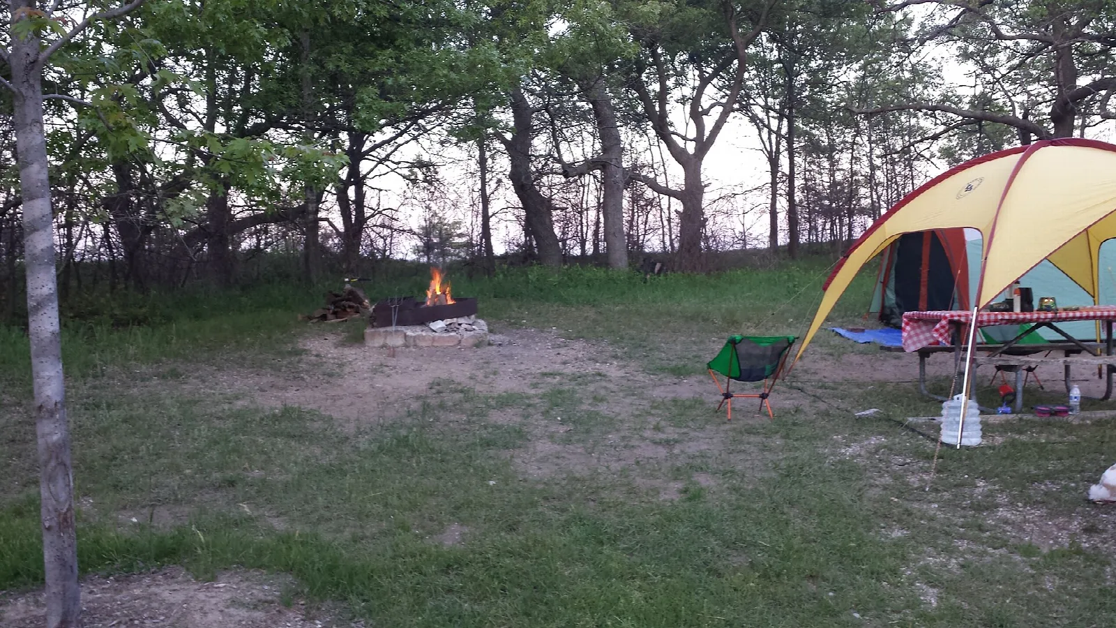 Tent and picnic table at a wooded campsite with a fire ring