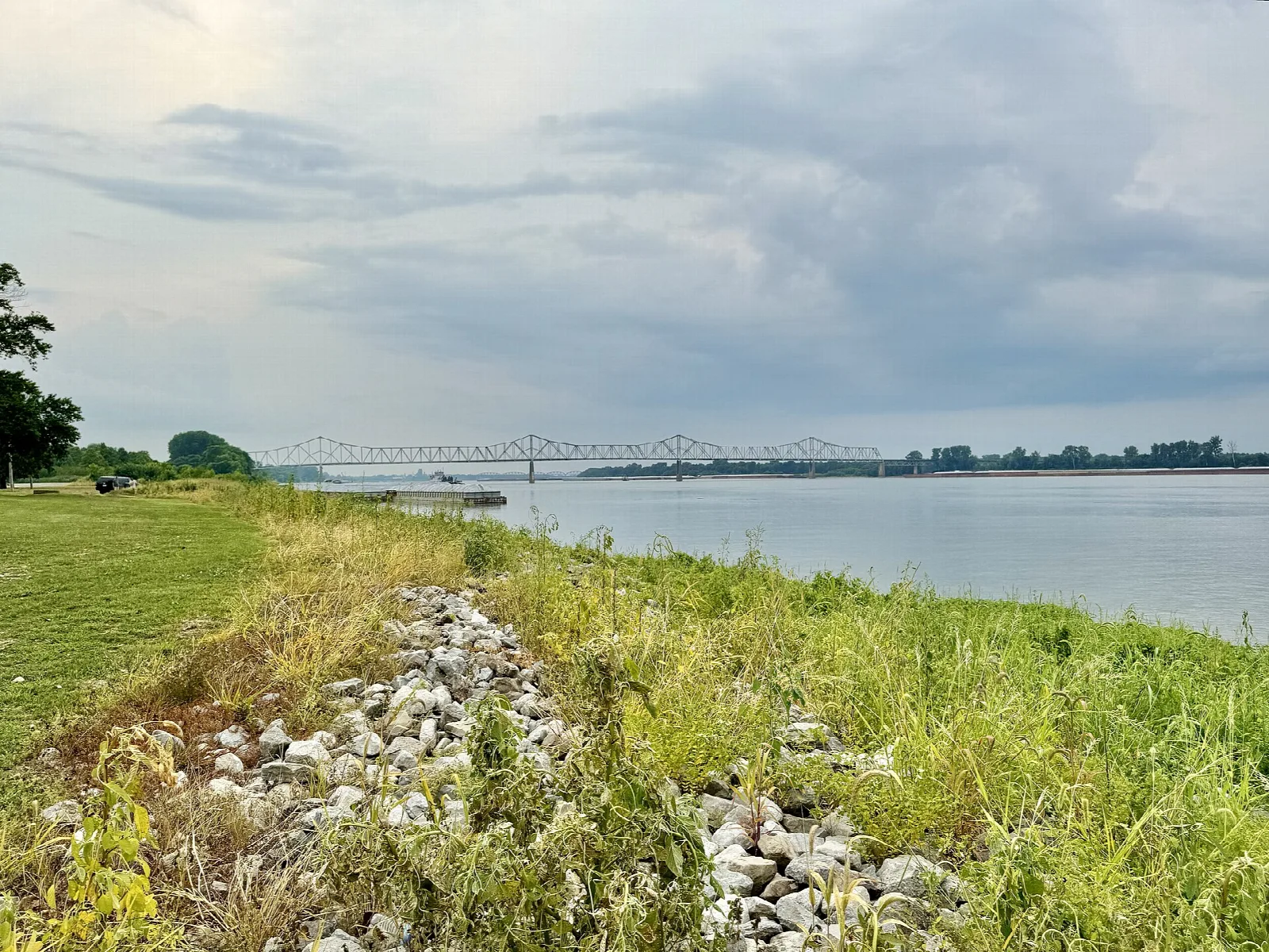 Rocky riverbank with grass and a bridge crossing the river