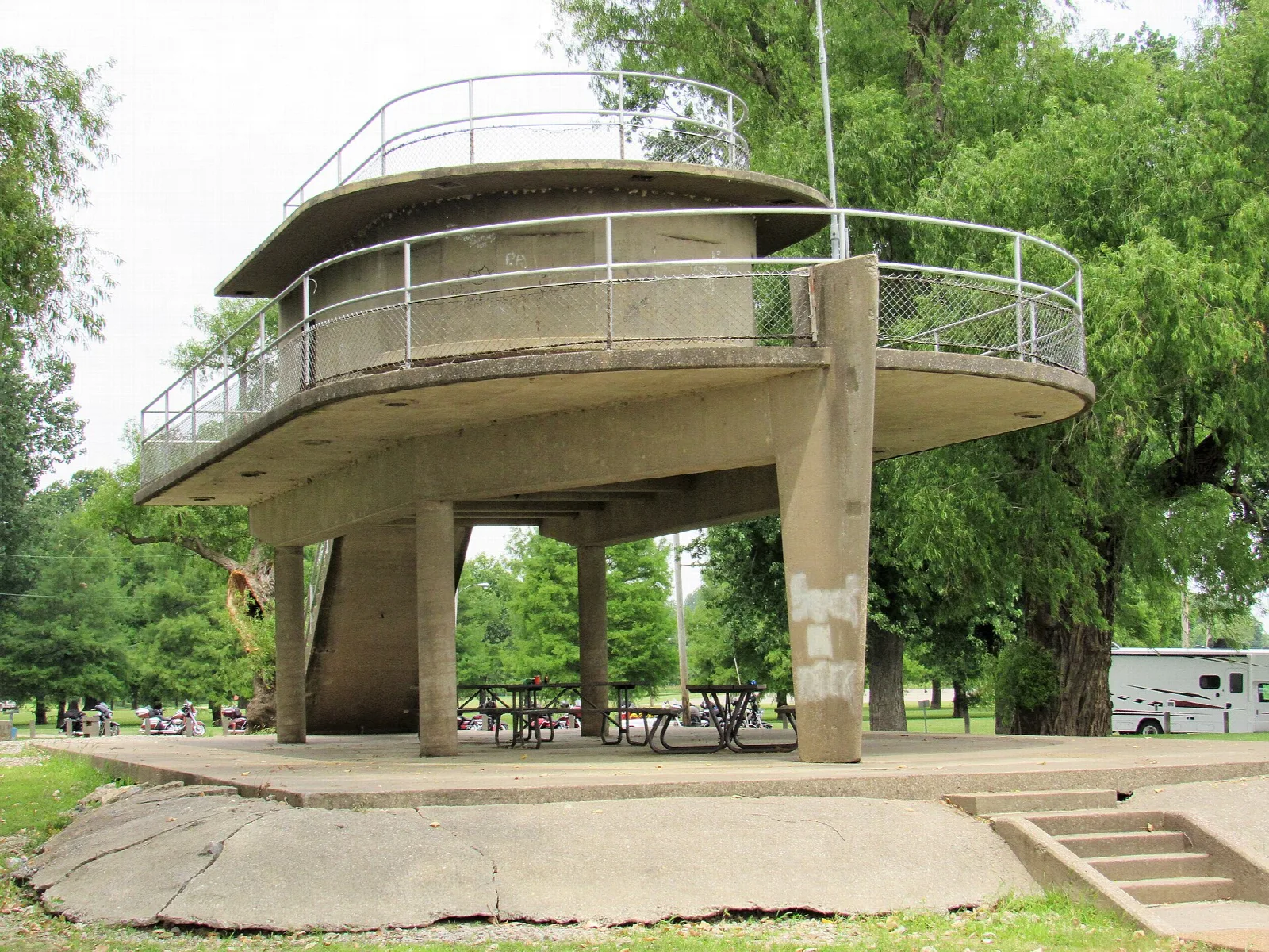 Round concrete lookout shelter with railings beside picnic tables and trees