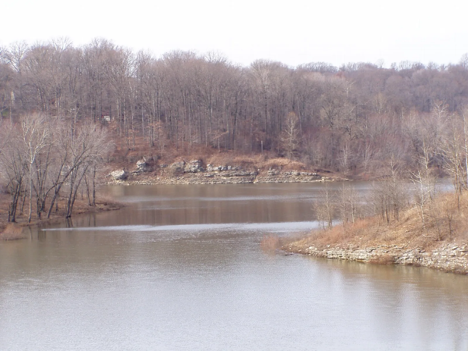 Calm reservoir with a rocky shore and bare winter trees