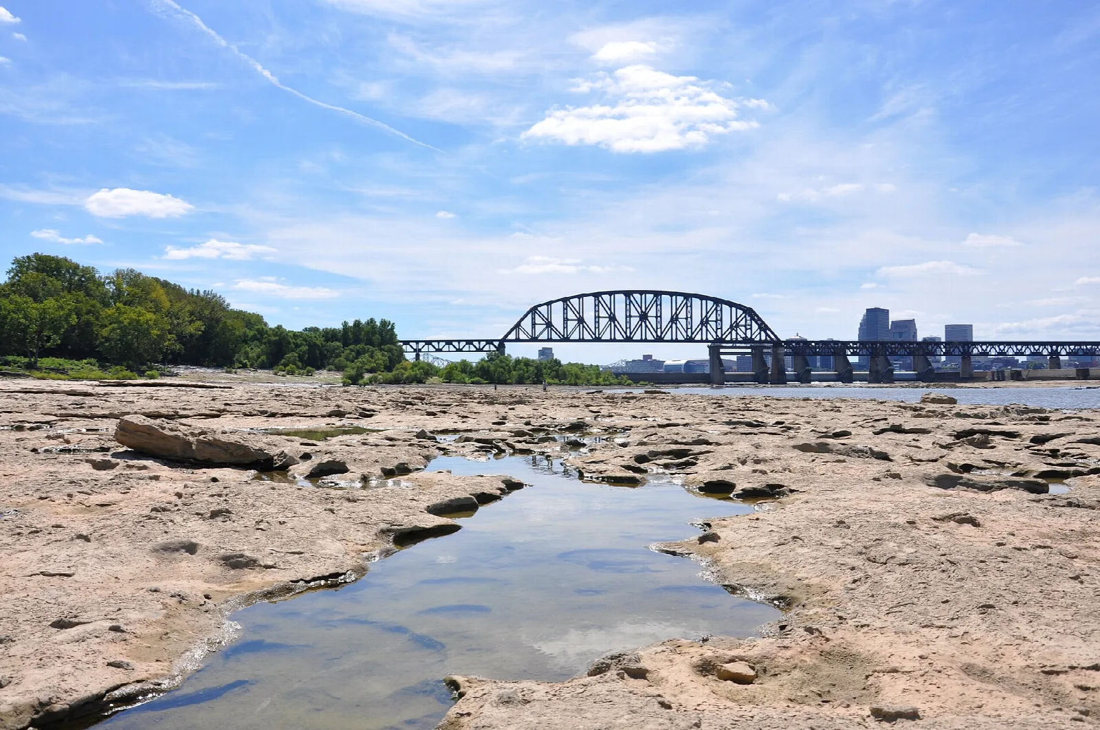 Flat cracked rock shelf with a shallow pool, a steel arch bridge beyond