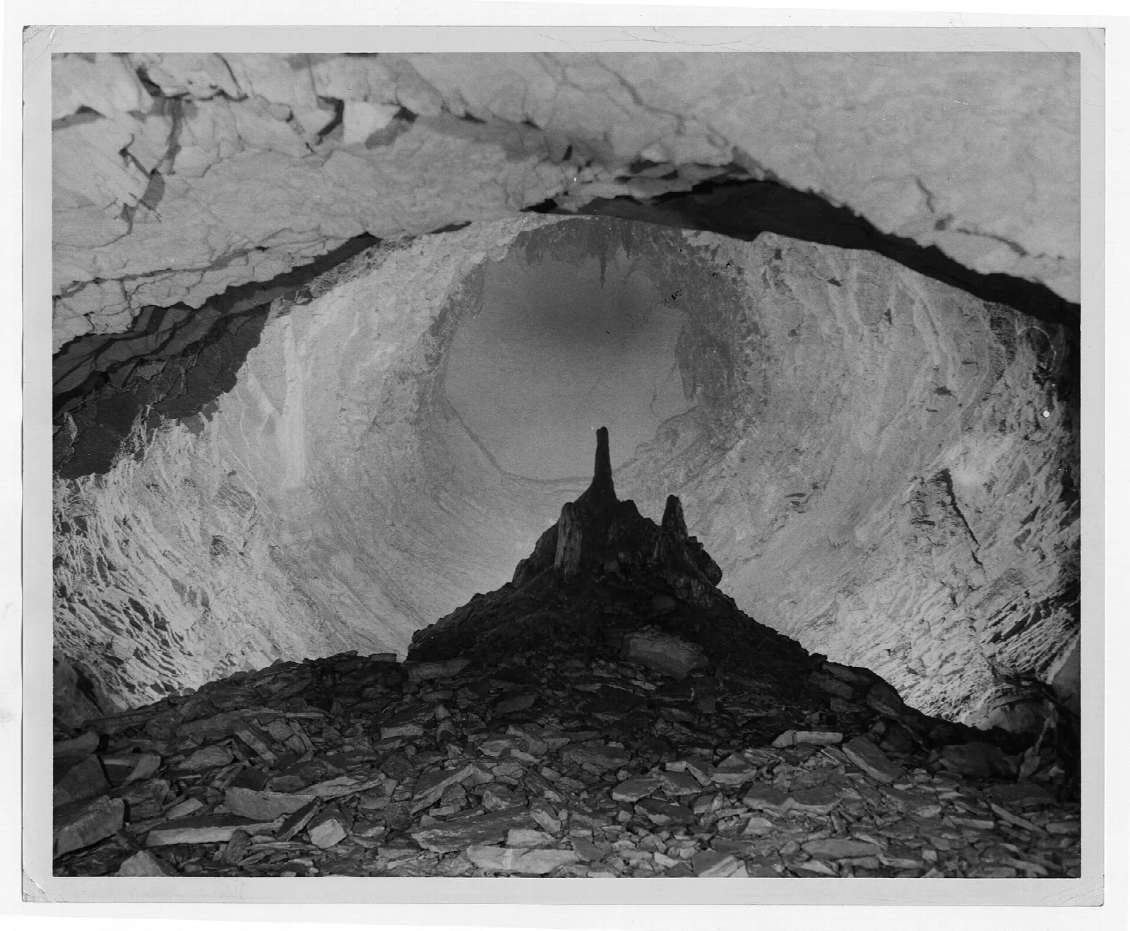 Black and white view inside a large cave chamber with a rock mound