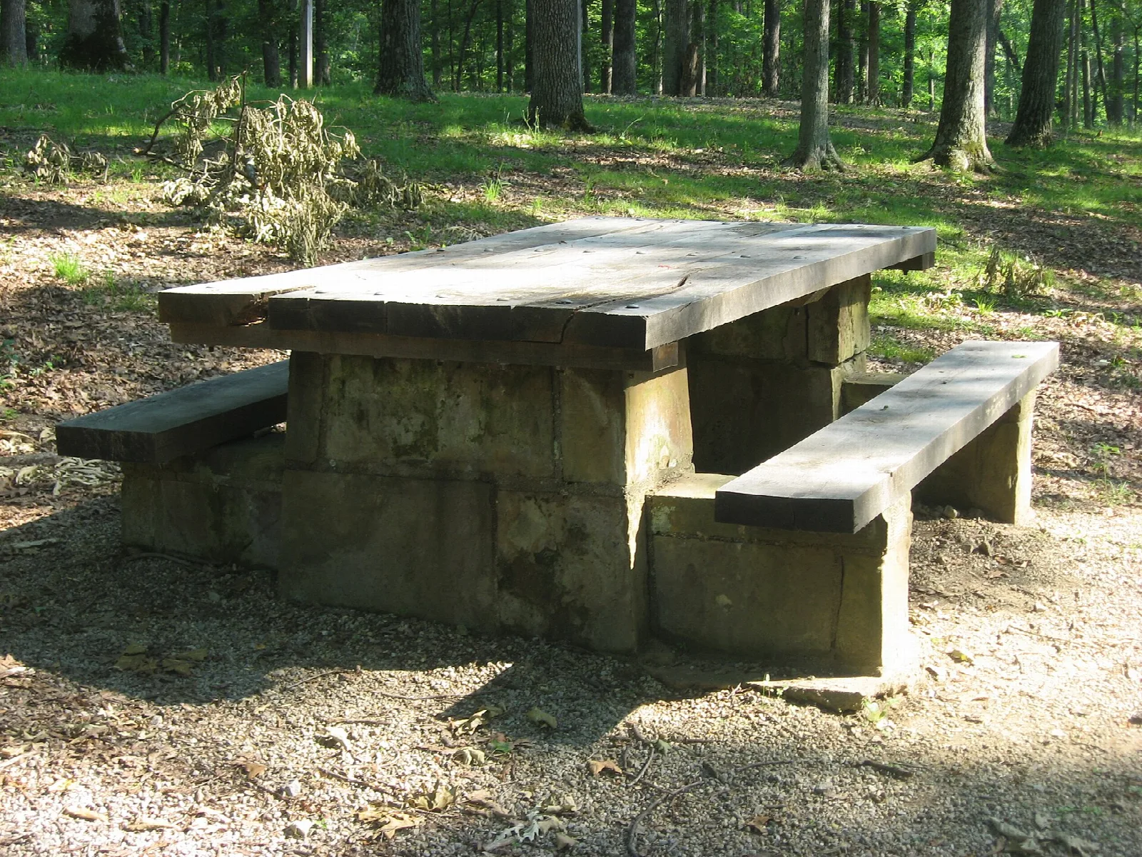 Stone picnic table with benches on a dirt clearing in the woods