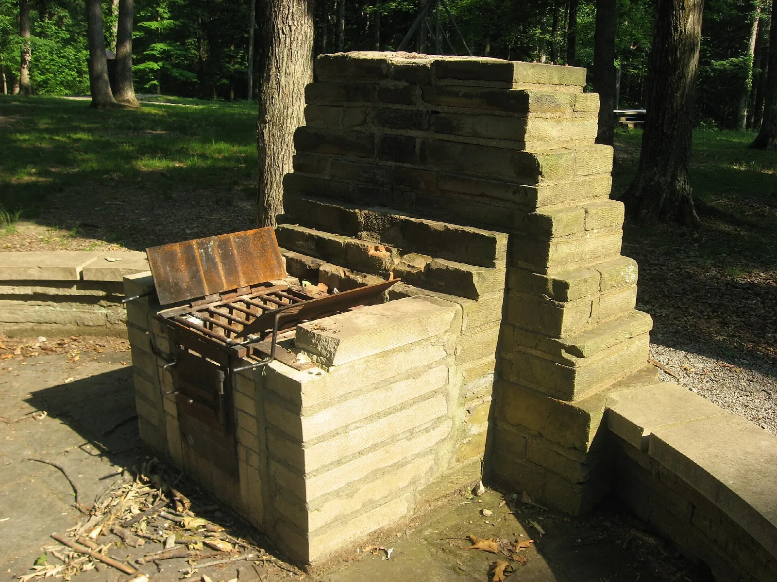 Large stacked-stone fireplace with a grill in a wooded picnic area