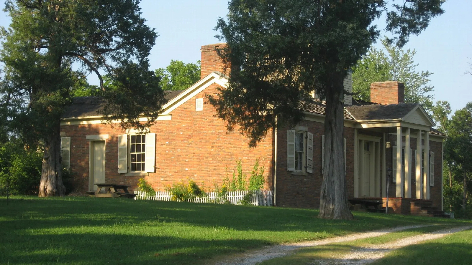 Two-story brick house with a porch and tall trees on a green lawn