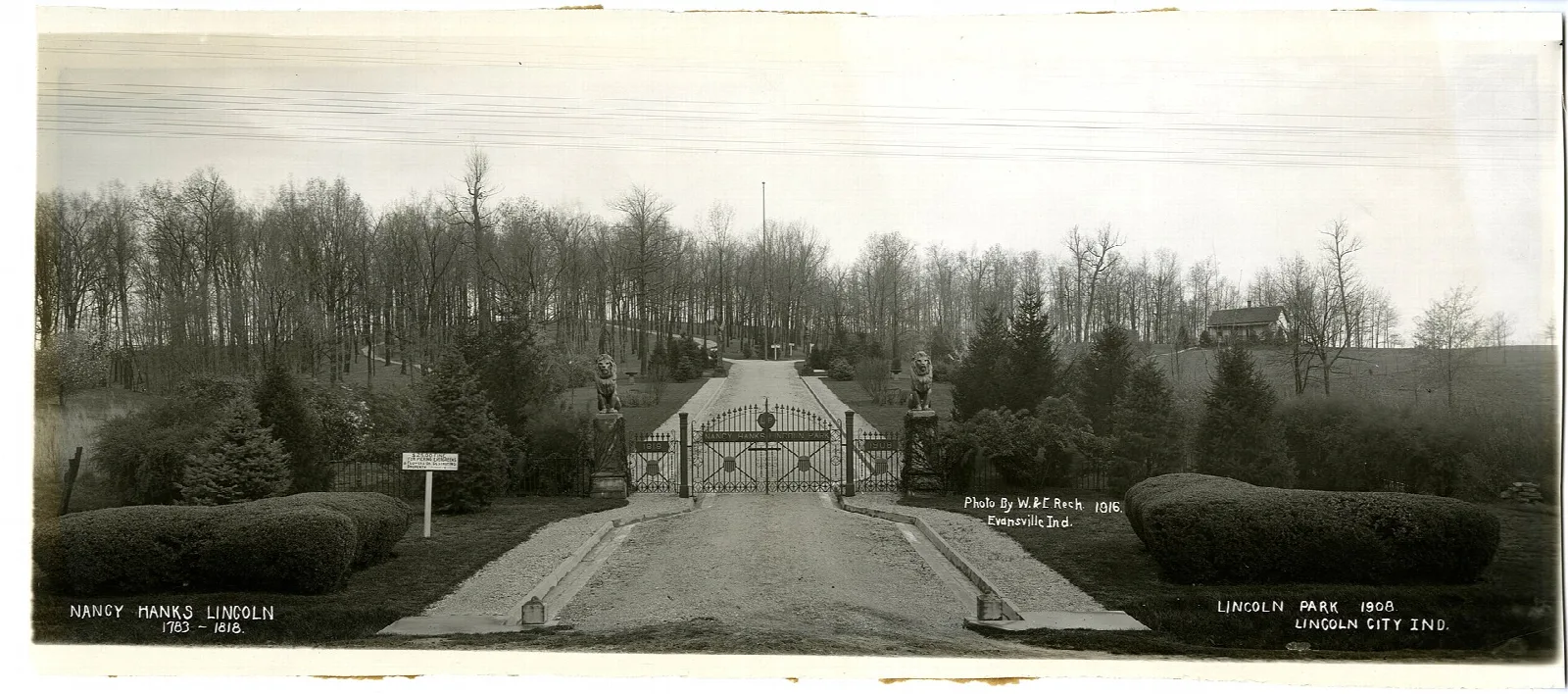 Old black-and-white view of a park entrance gate and road lined with shrubs
