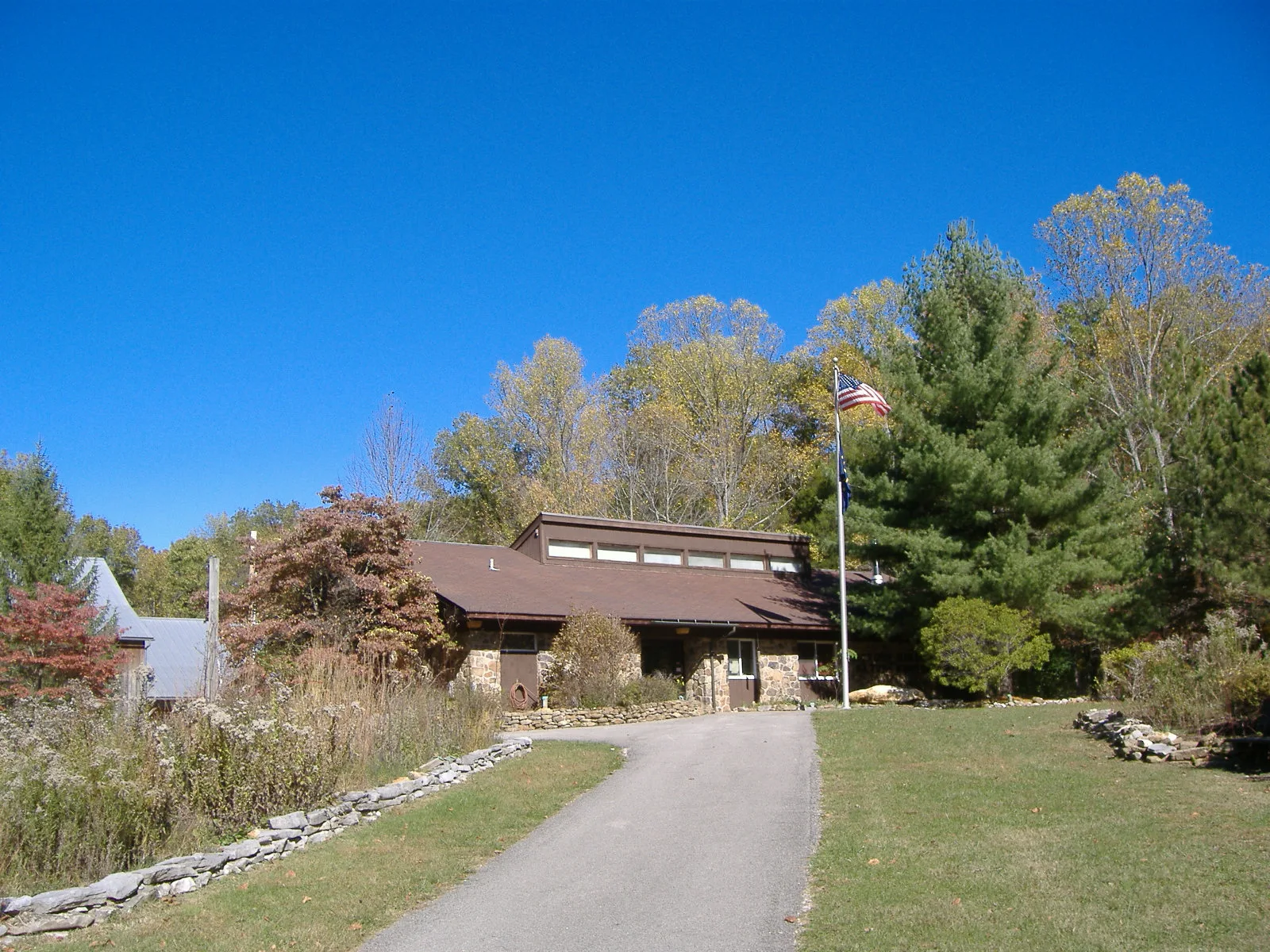 Low brown building with a flagpole beside a path and fall trees