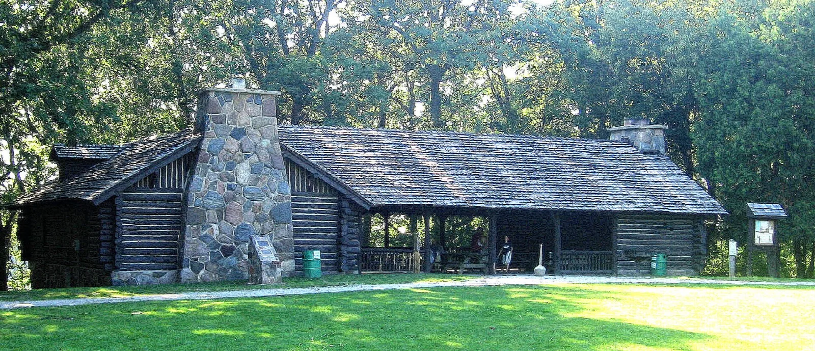 Log and stone picnic shelter with a stone chimney on a green lawn