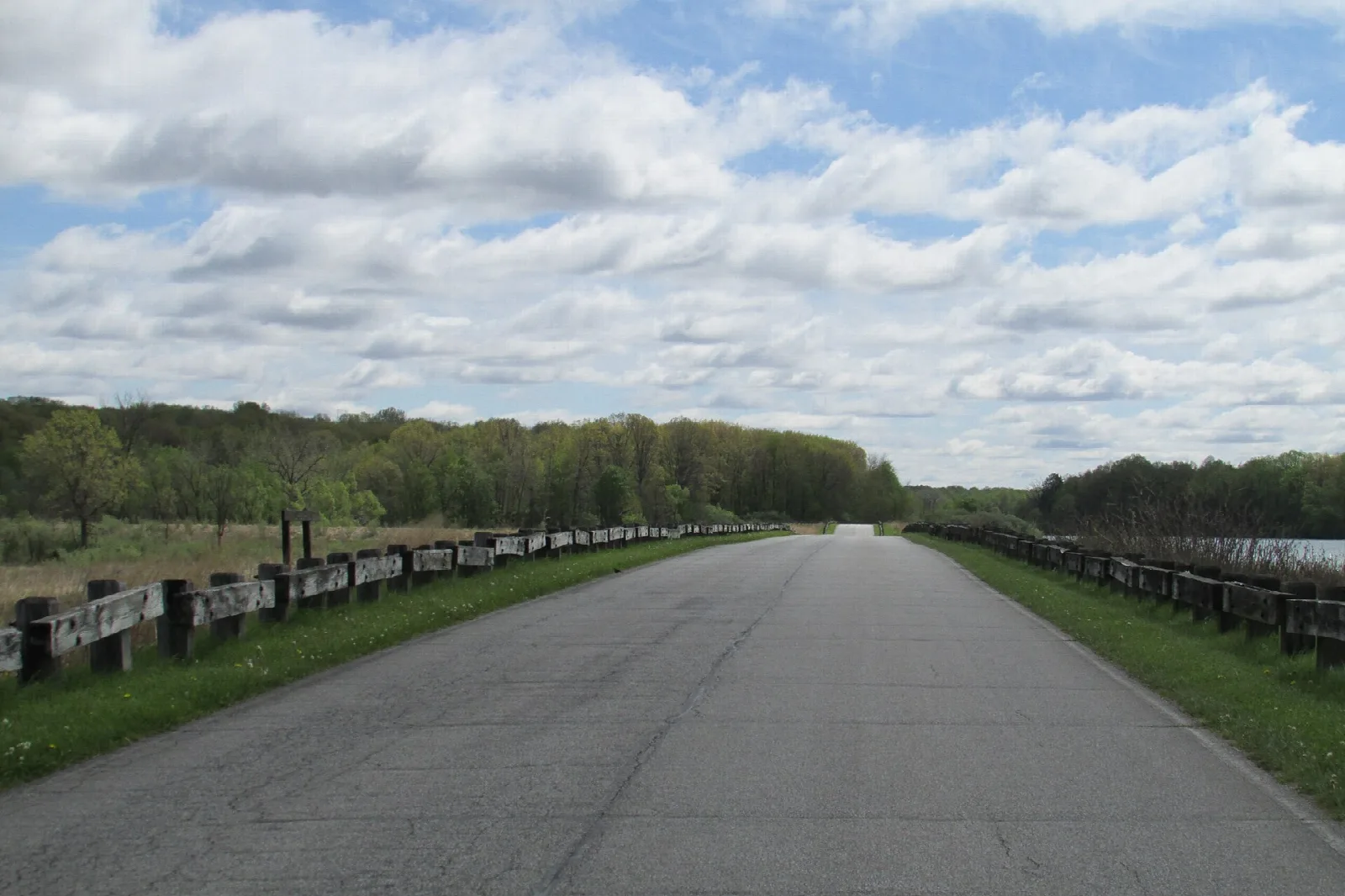 Paved road with a wooden rail running along a dam under a cloudy blue sky