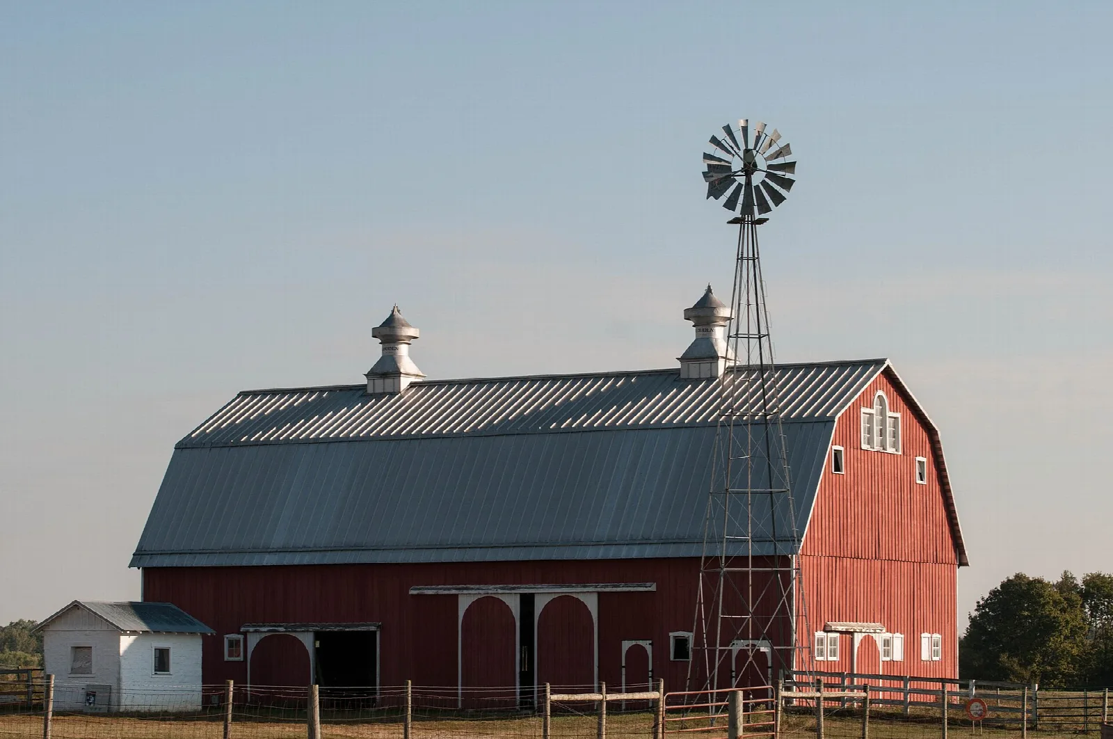 Large red barn with a windmill tower against a pale sky