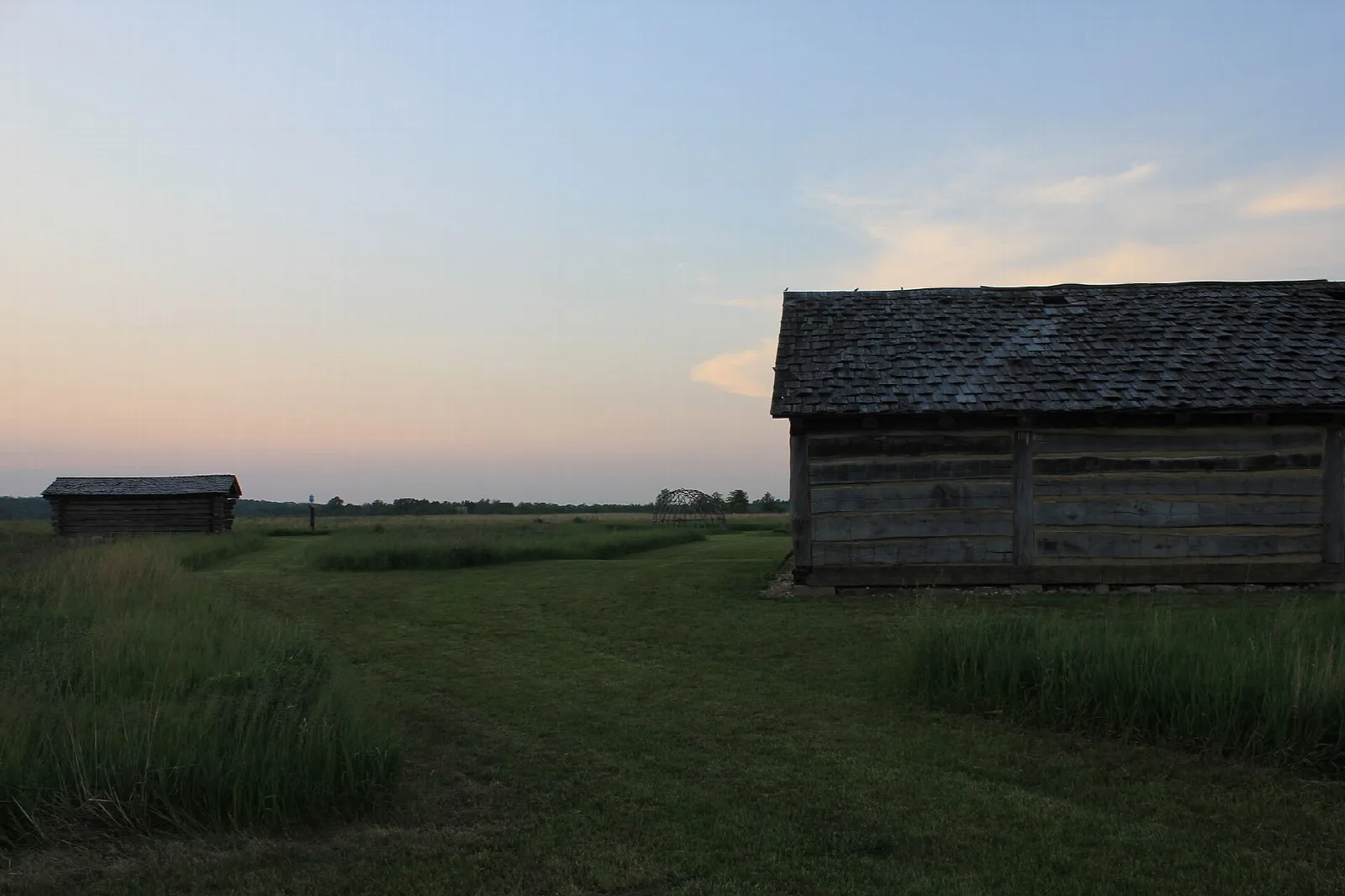 Weathered wooden cabin in a mown grass field at dusk
