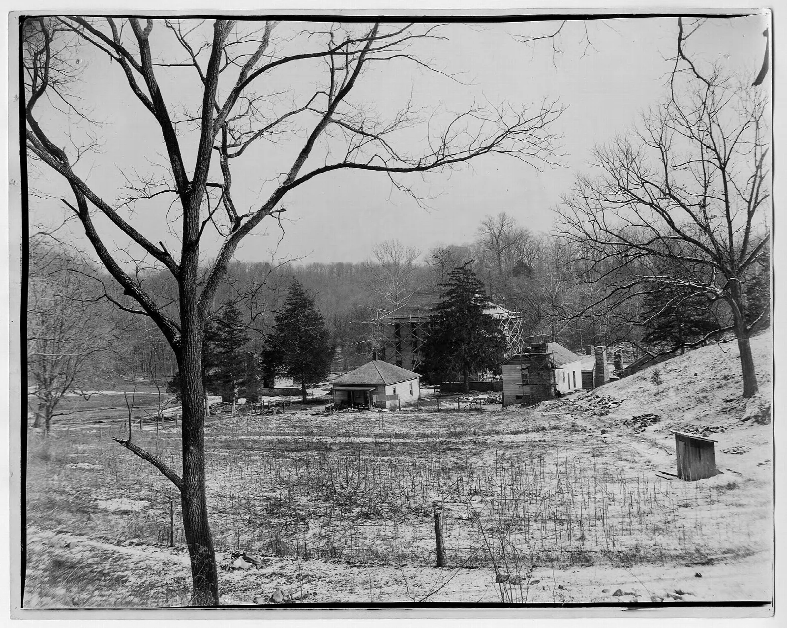 Black and white view of a snowy valley with small buildings among bare trees