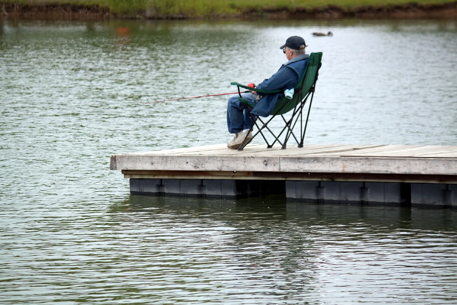 Person in a camp chair fishing from a wooden dock on a lake