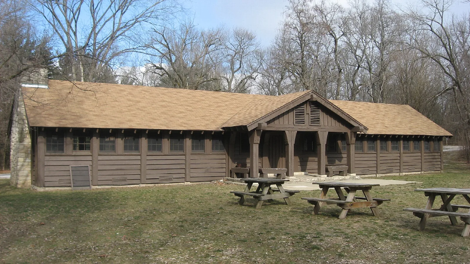 Long brown wooden lodge with a low roof and picnic tables on the lawn