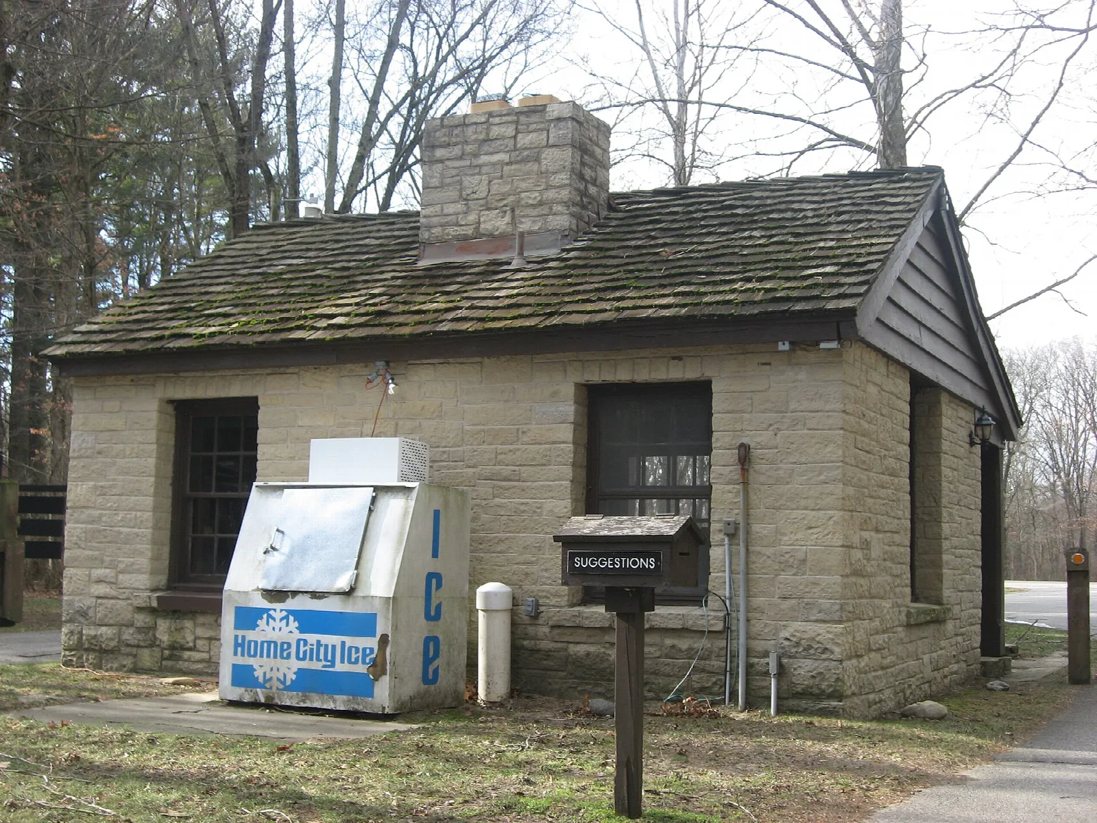 Small stone gatehouse with a stone chimney among bare trees