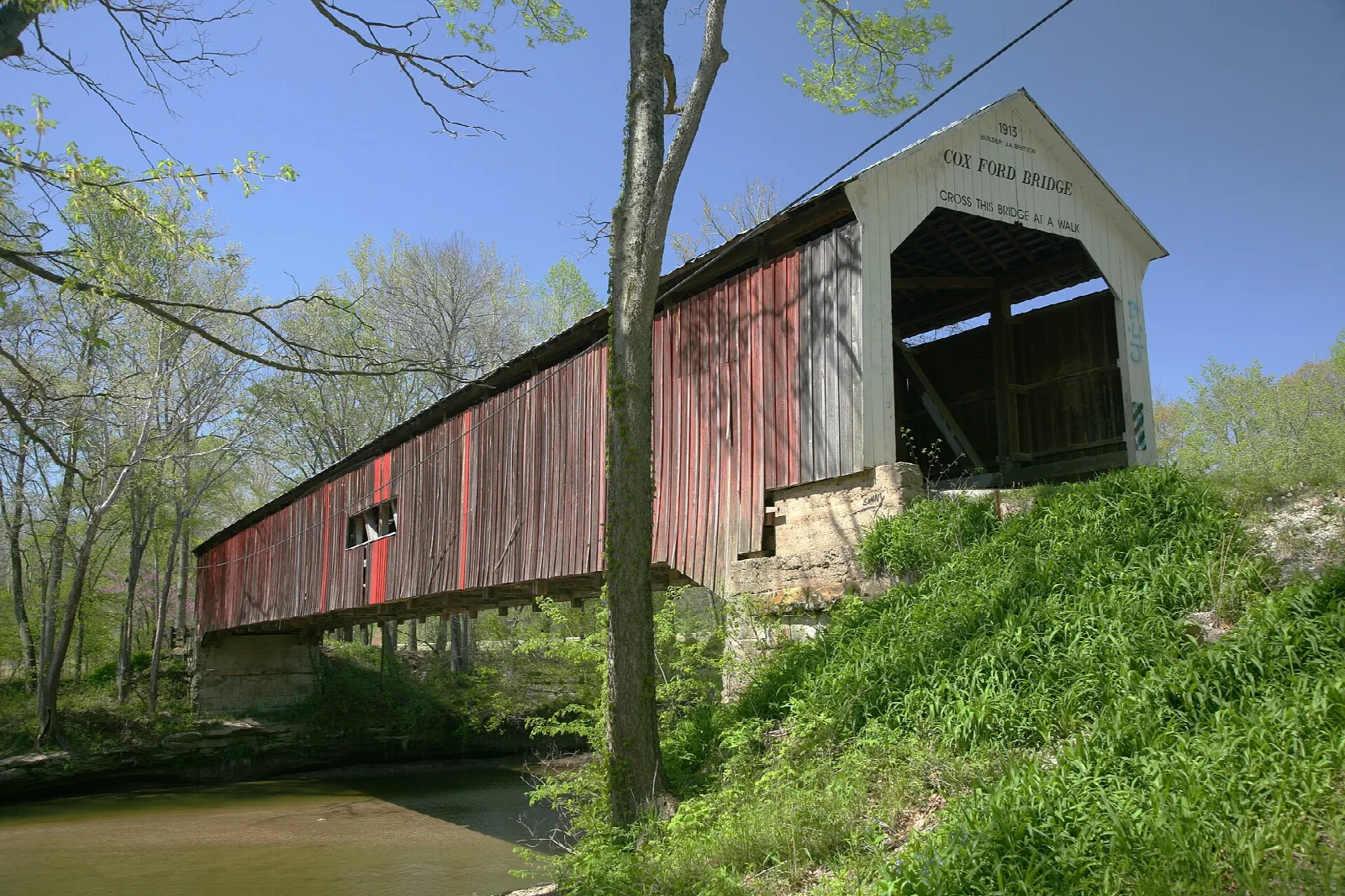 Red covered bridge with a stone base beside green grassy banks