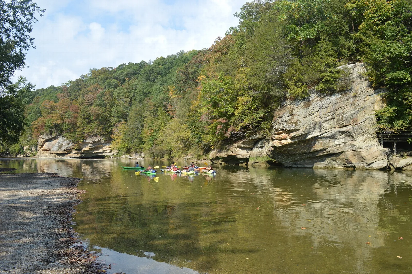 Sandstone cliff above a river bend with kayaks, under autumn-colored trees
