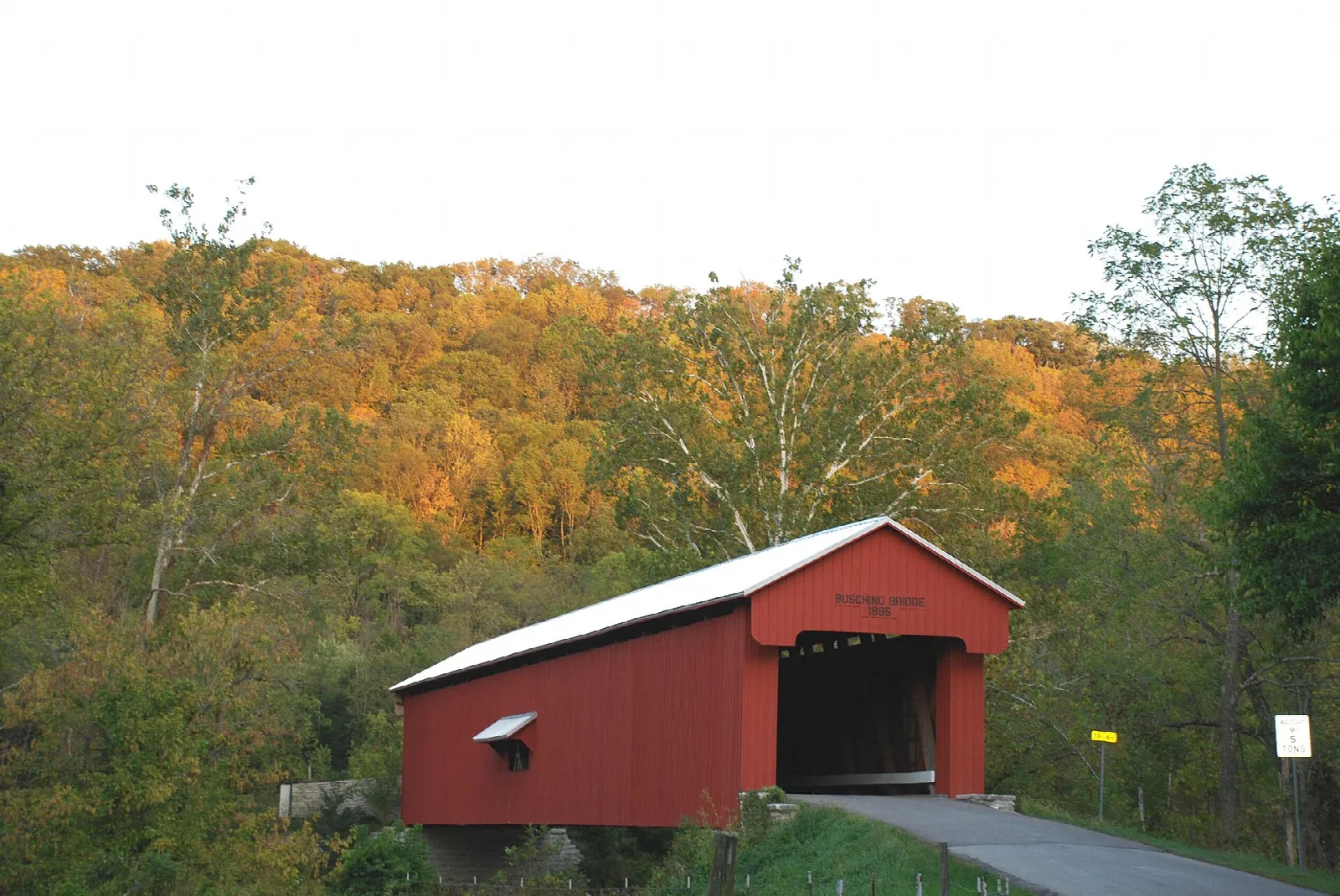Red covered bridge in front of hills with autumn-colored trees