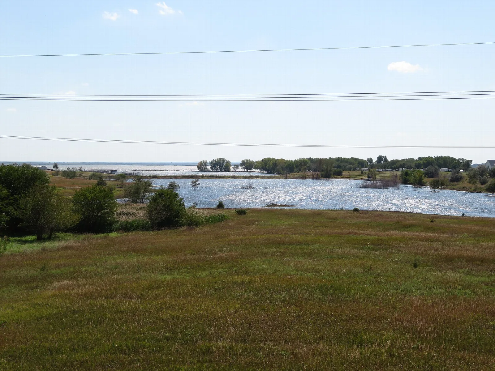 Grassy field in the foreground and a lake with trees and a far shore