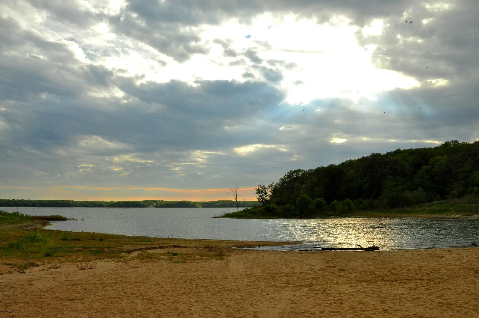 Sandy lake beach with a wooded point and a sky of breaking clouds