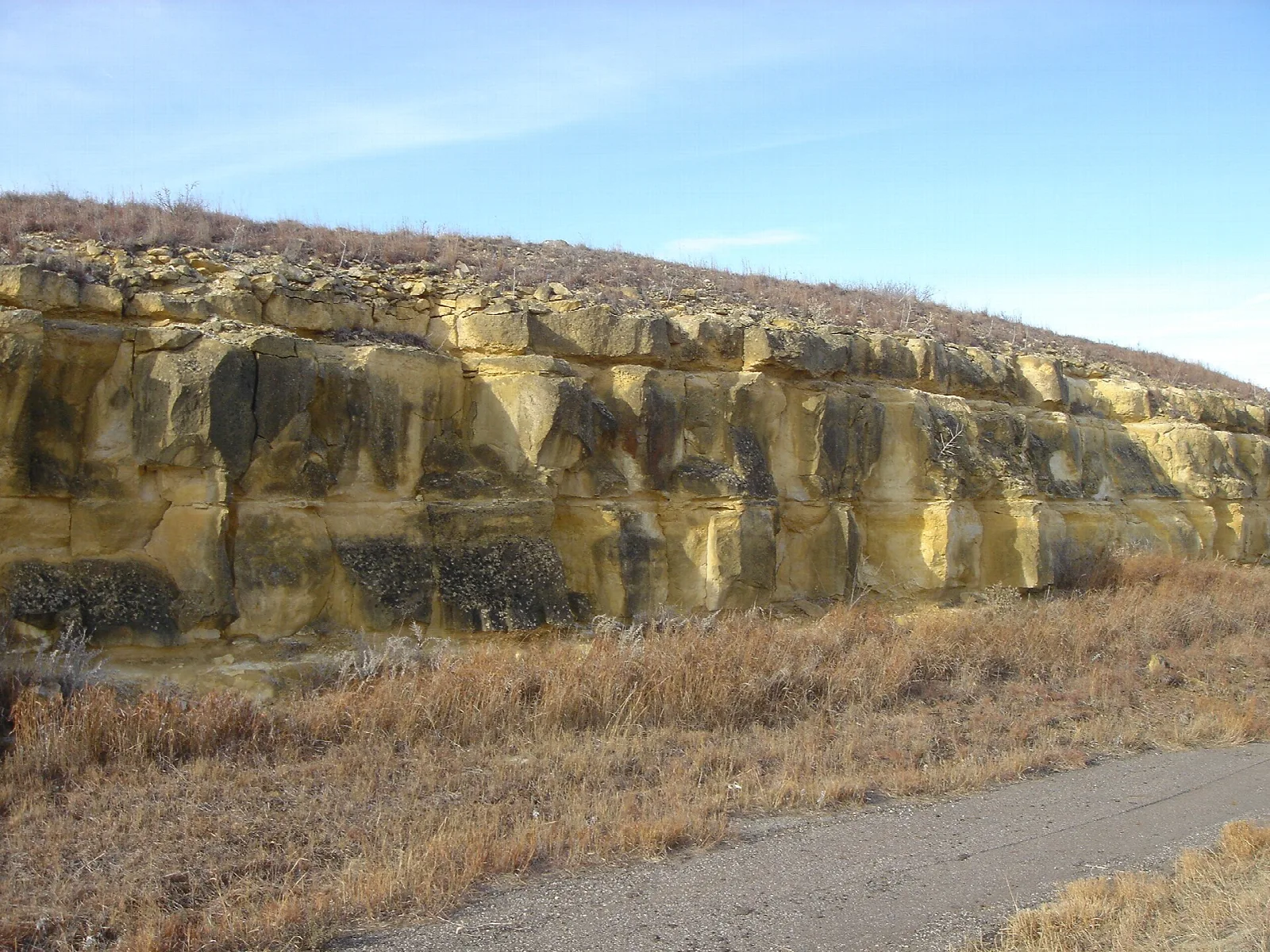 Yellow limestone ledge above a gravel path under a blue sky