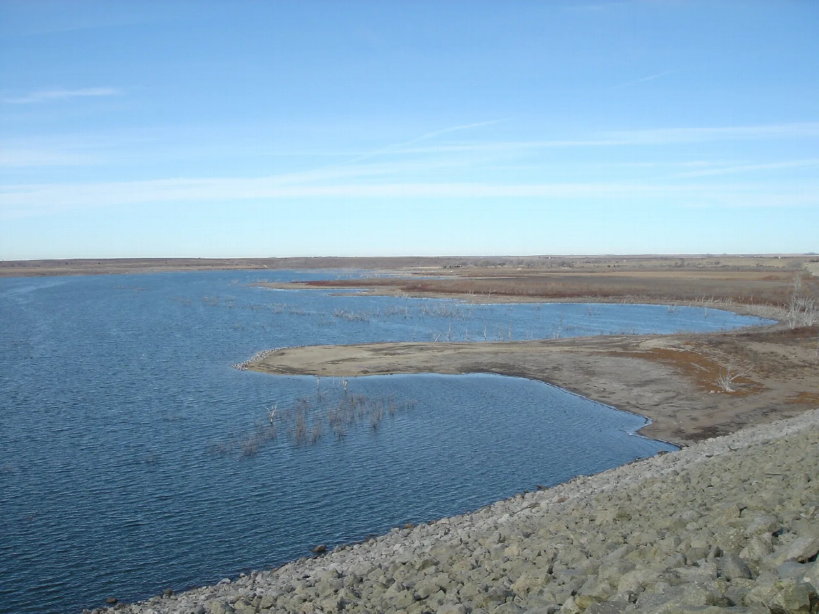 Wide blue reservoir with a gravel shoreline and a low far bank