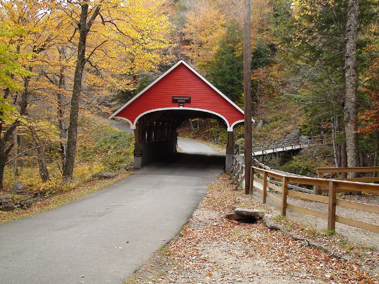 Red covered bridge over a paved path in autumn woods