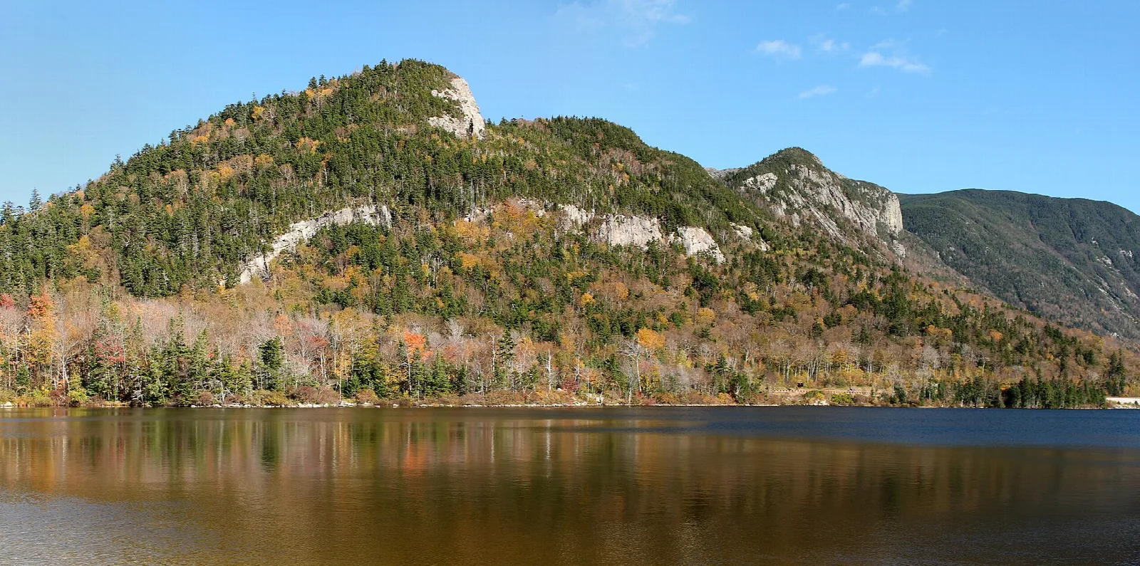 Forested cliff-topped mountain above a still lake in autumn