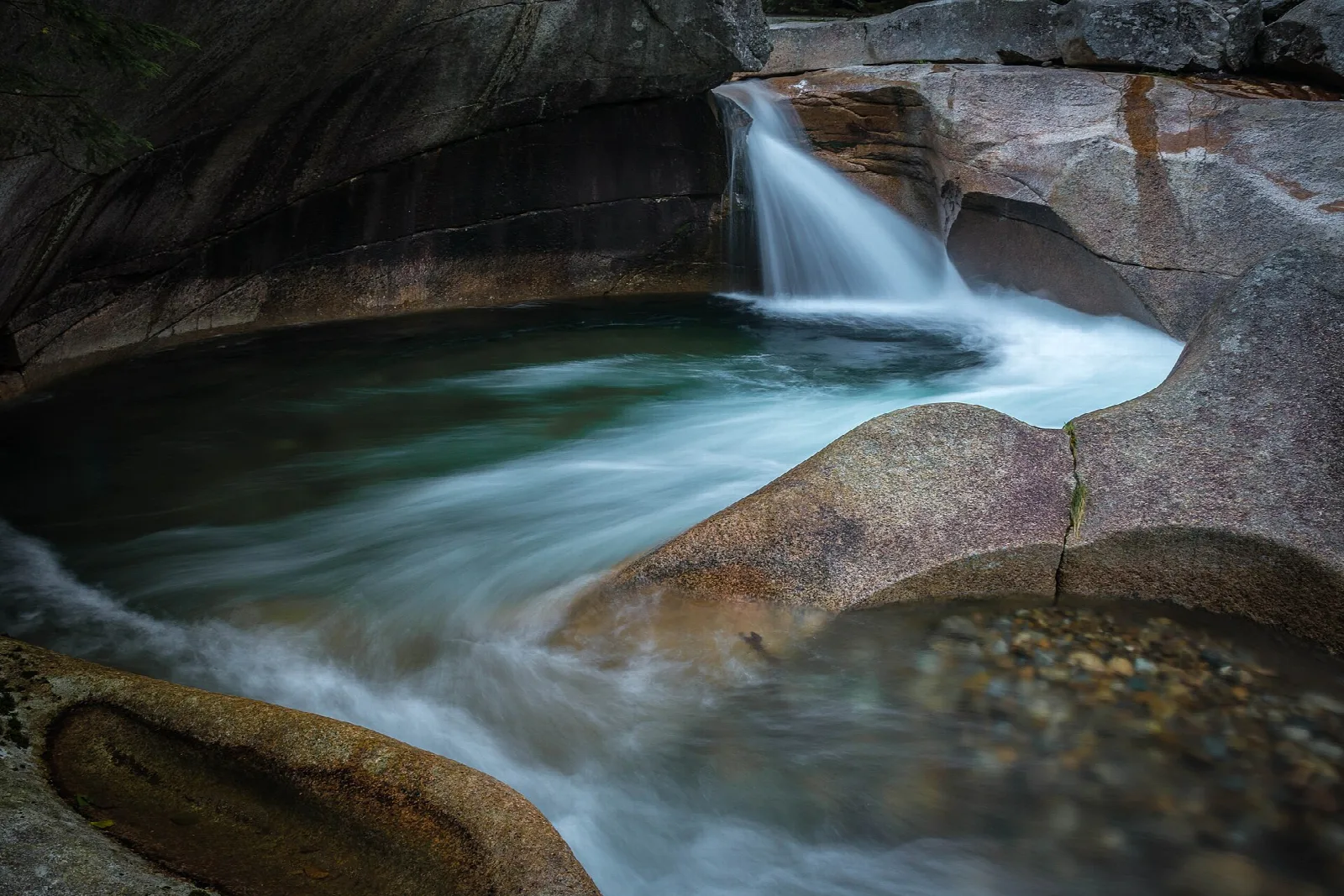 Waterfall pouring into a round granite pool in a rock gorge