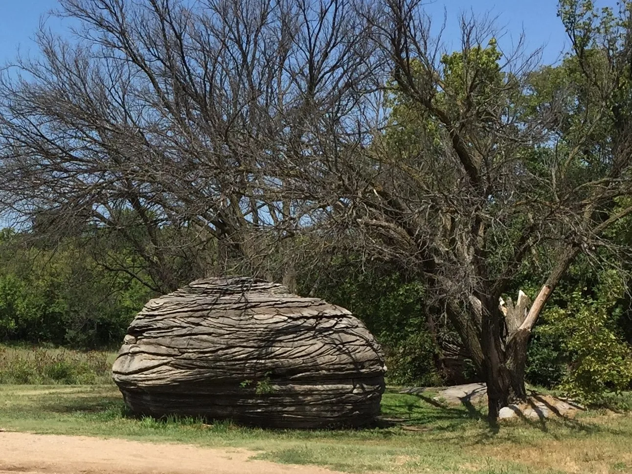 A rounded layered boulder beside a dirt path and bare trees