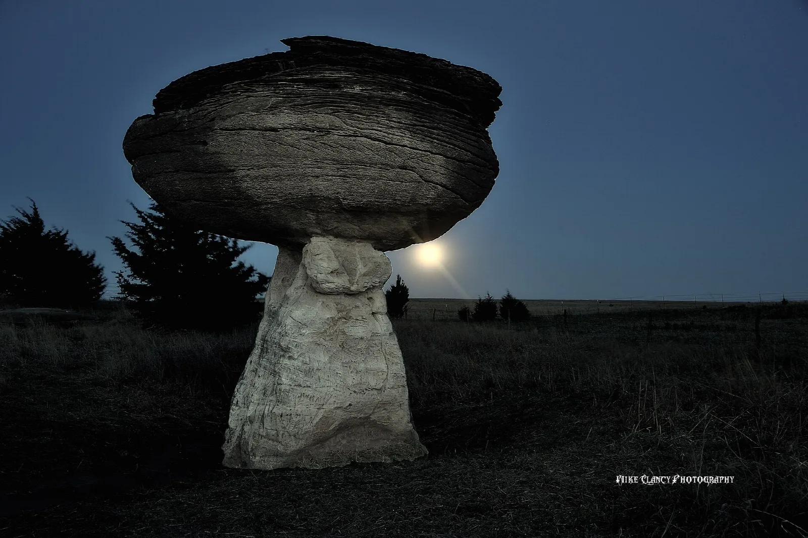 A large mushroom-shaped sandstone rock lit against a dark sky with a moonrise