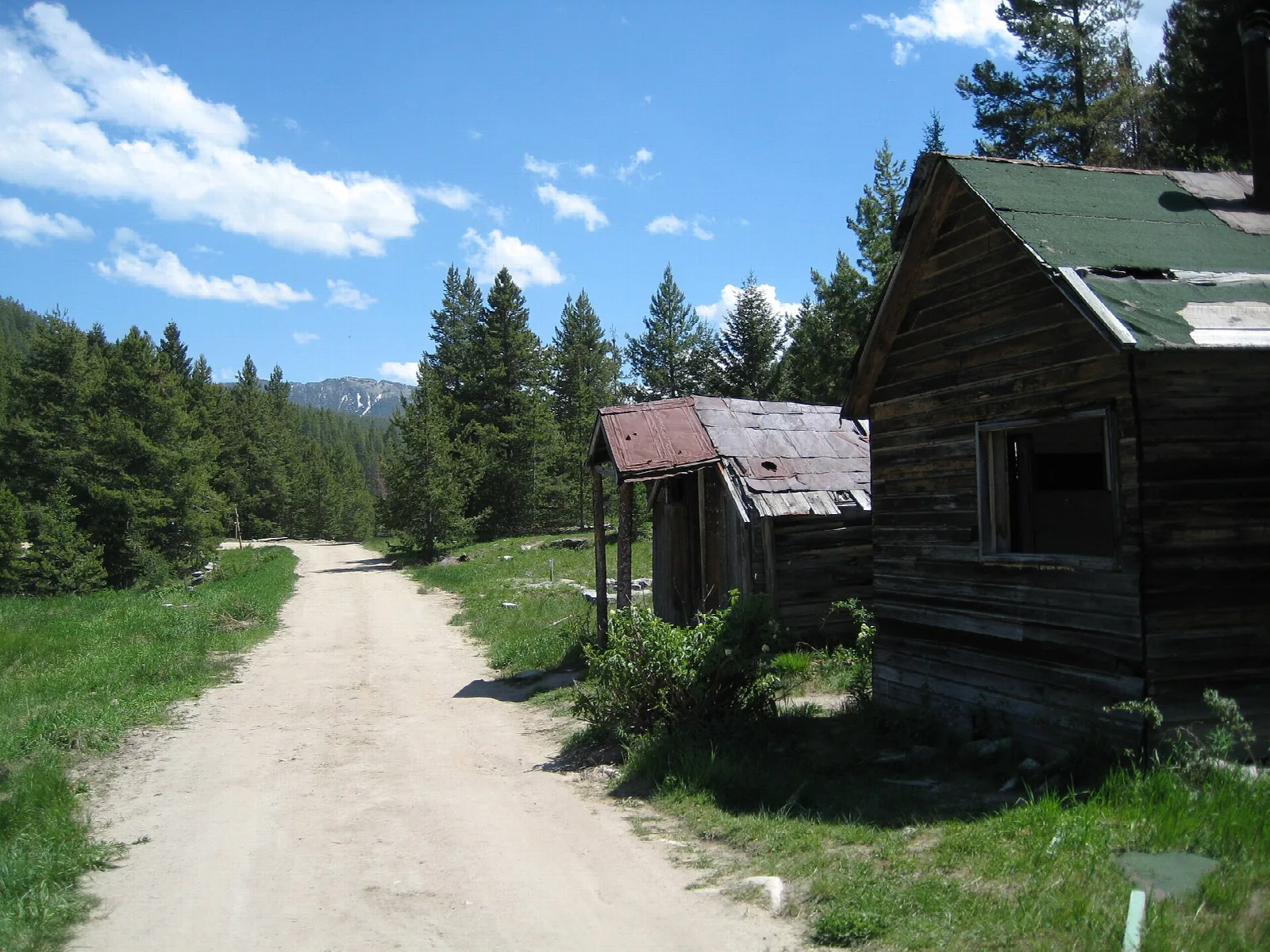 Dirt road running between weathered log buildings and pine trees