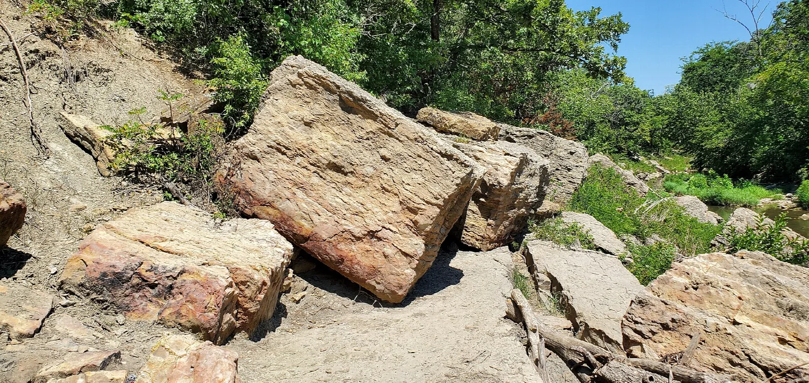Large tan limestone blocks slumped down a slope beside a creek, with green trees