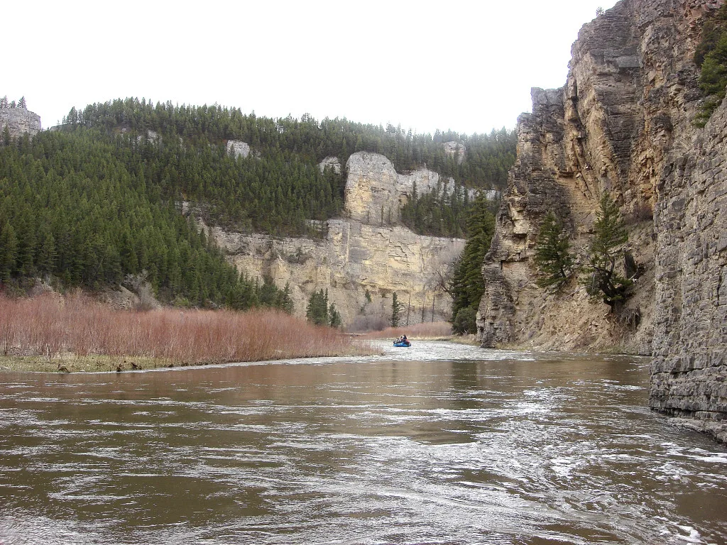 Brown river winding between steep rock cliffs and forested slopes