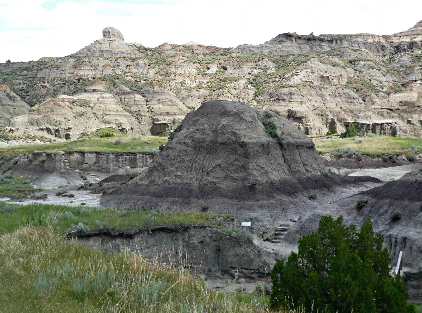 Dark dome-shaped badland hill below pale eroded ridges