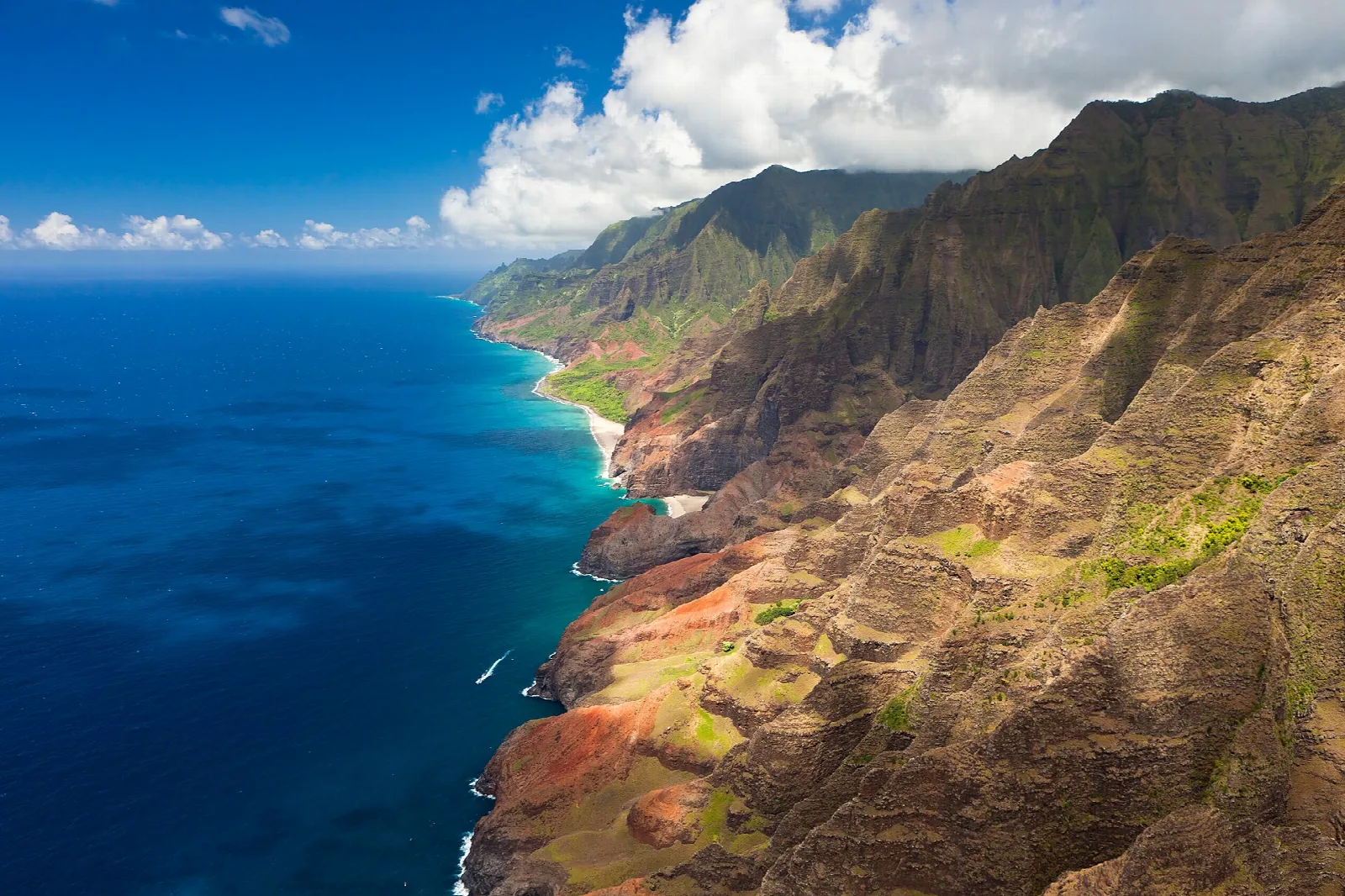 Aerial view of red-and-green cliffs dropping to deep blue ocean along the coast