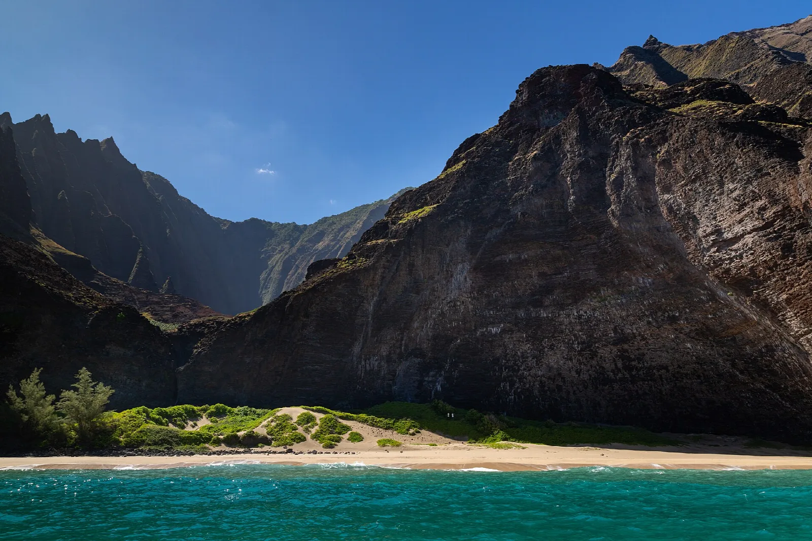 Sandy beach and green grass at the foot of dark sea cliffs, with turquoise water