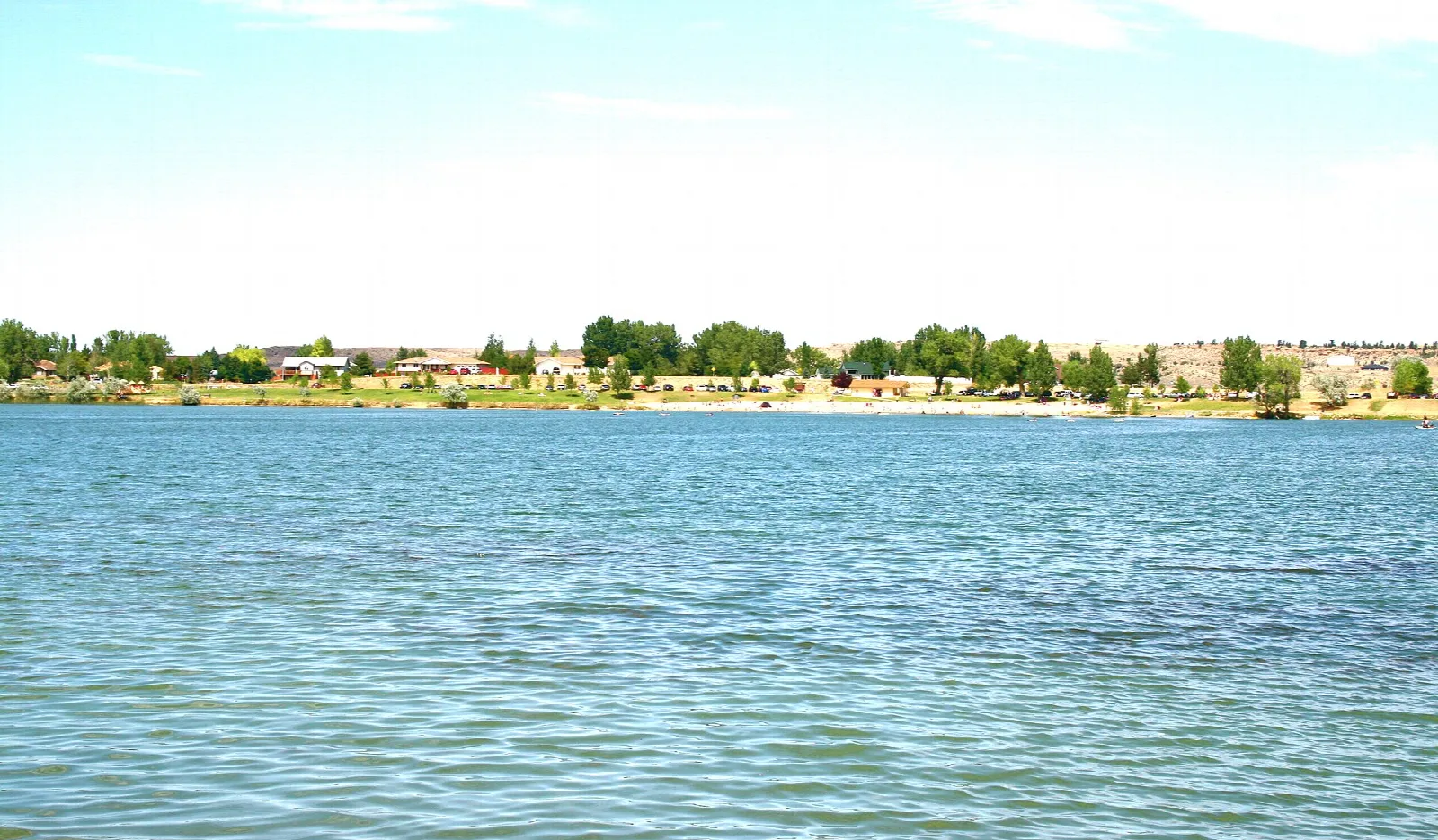 Wide blue lake with a tree-lined shore and buildings in the distance