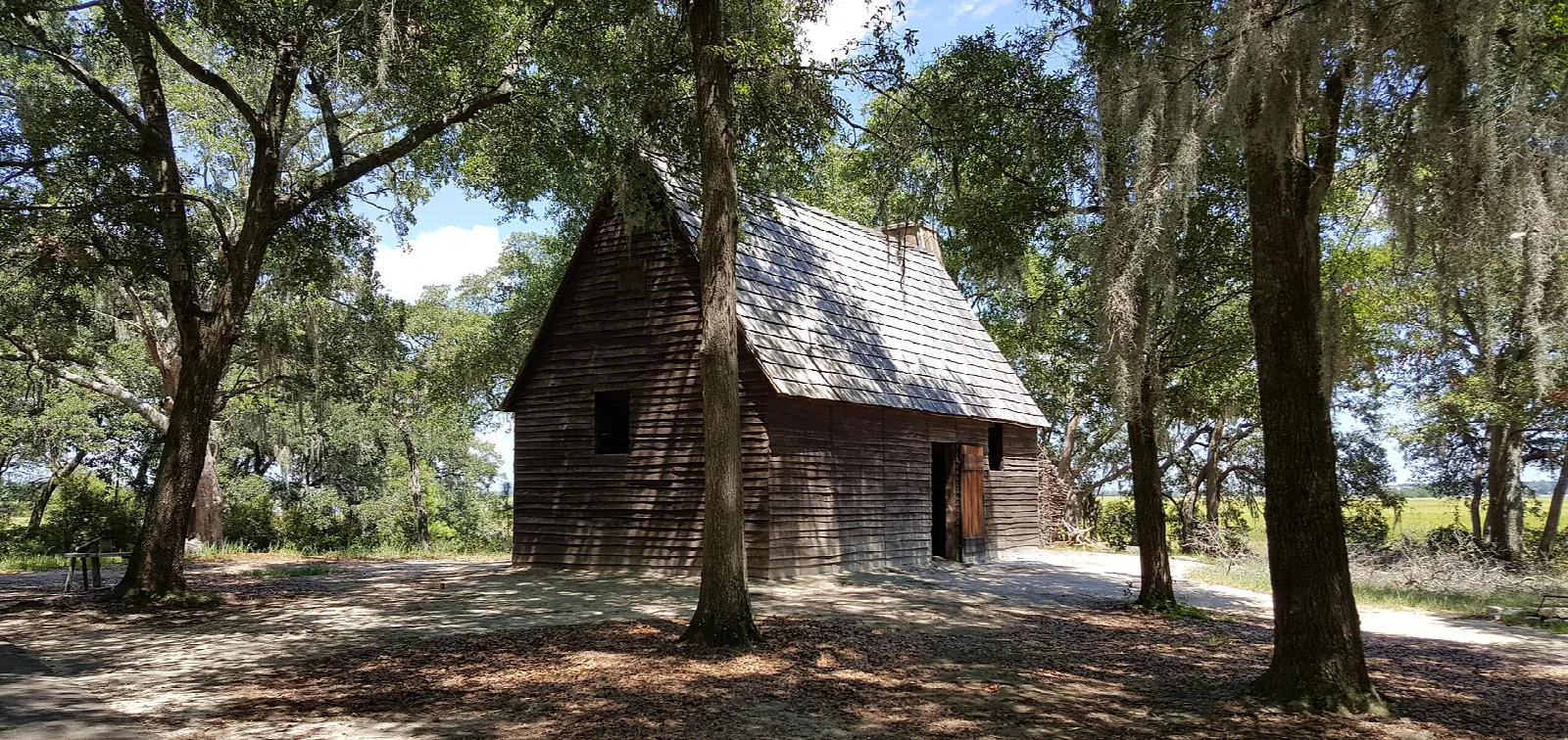 Small wooden cabin with a shingled roof under large oak trees