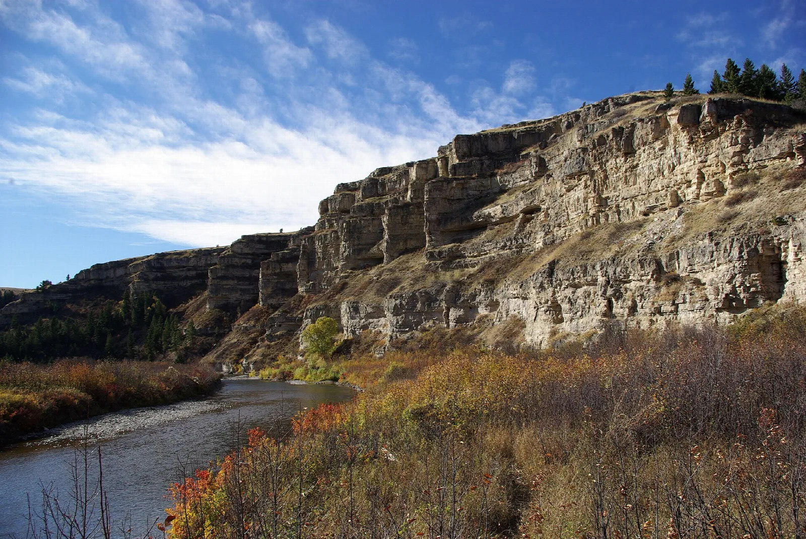 Creek winding below tall tan limestone cliffs with autumn-colored brush