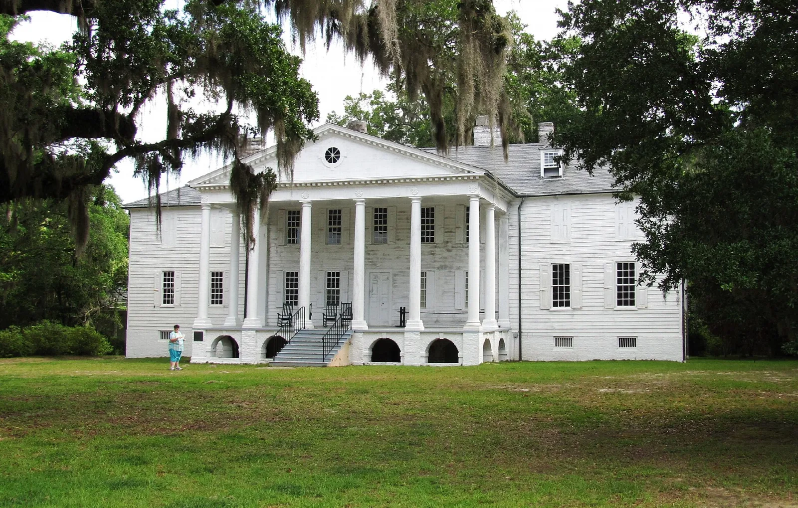 White columned plantation house seen across a lawn under live oaks
