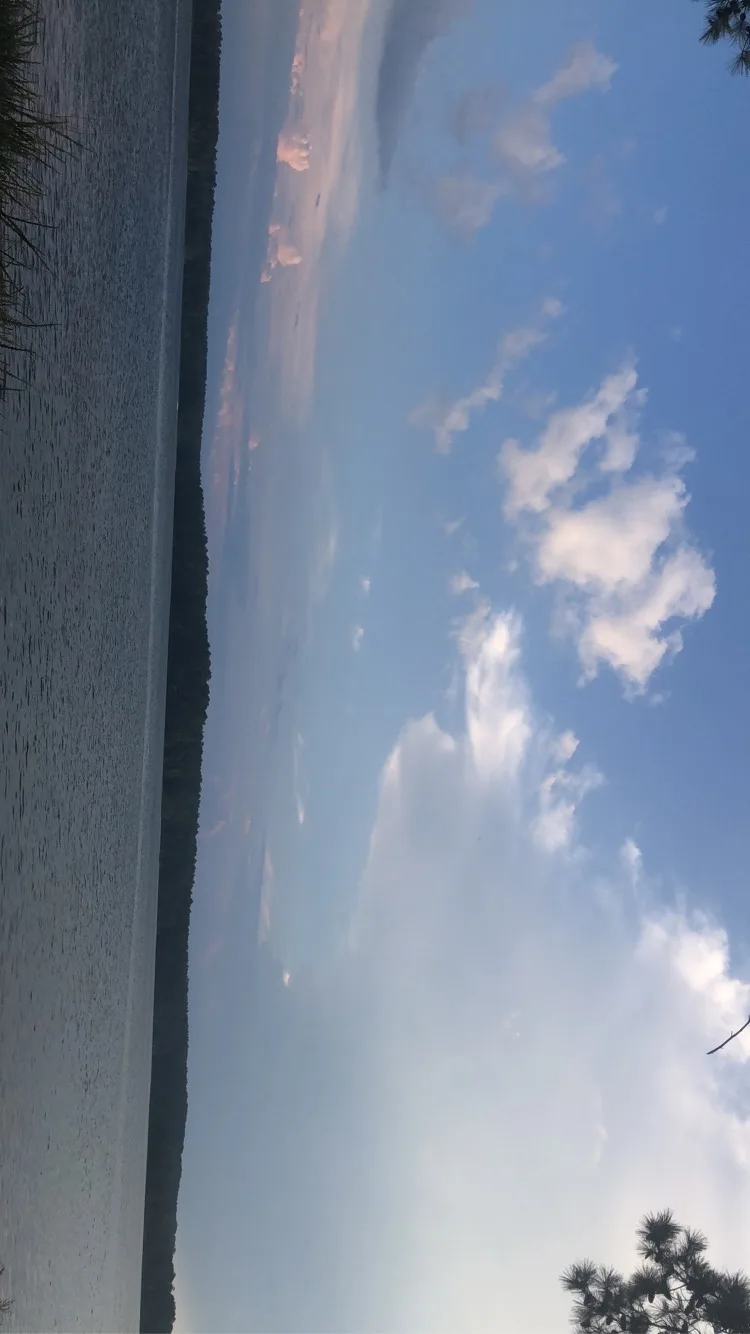 Wide lake under a blue sky with scattered clouds and a wooded far shore