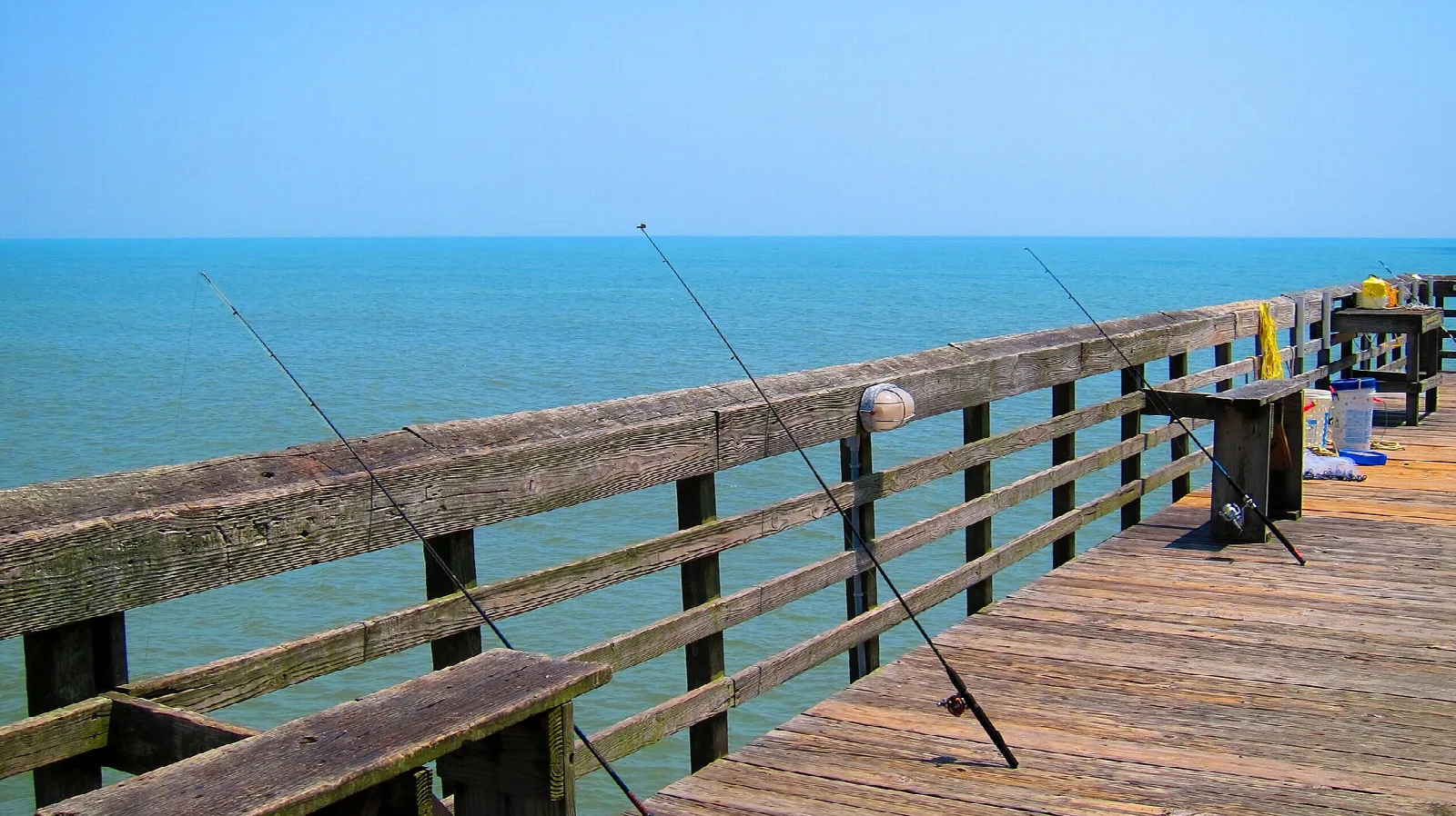 Wooden pier railing with fishing rods leaning over the ocean